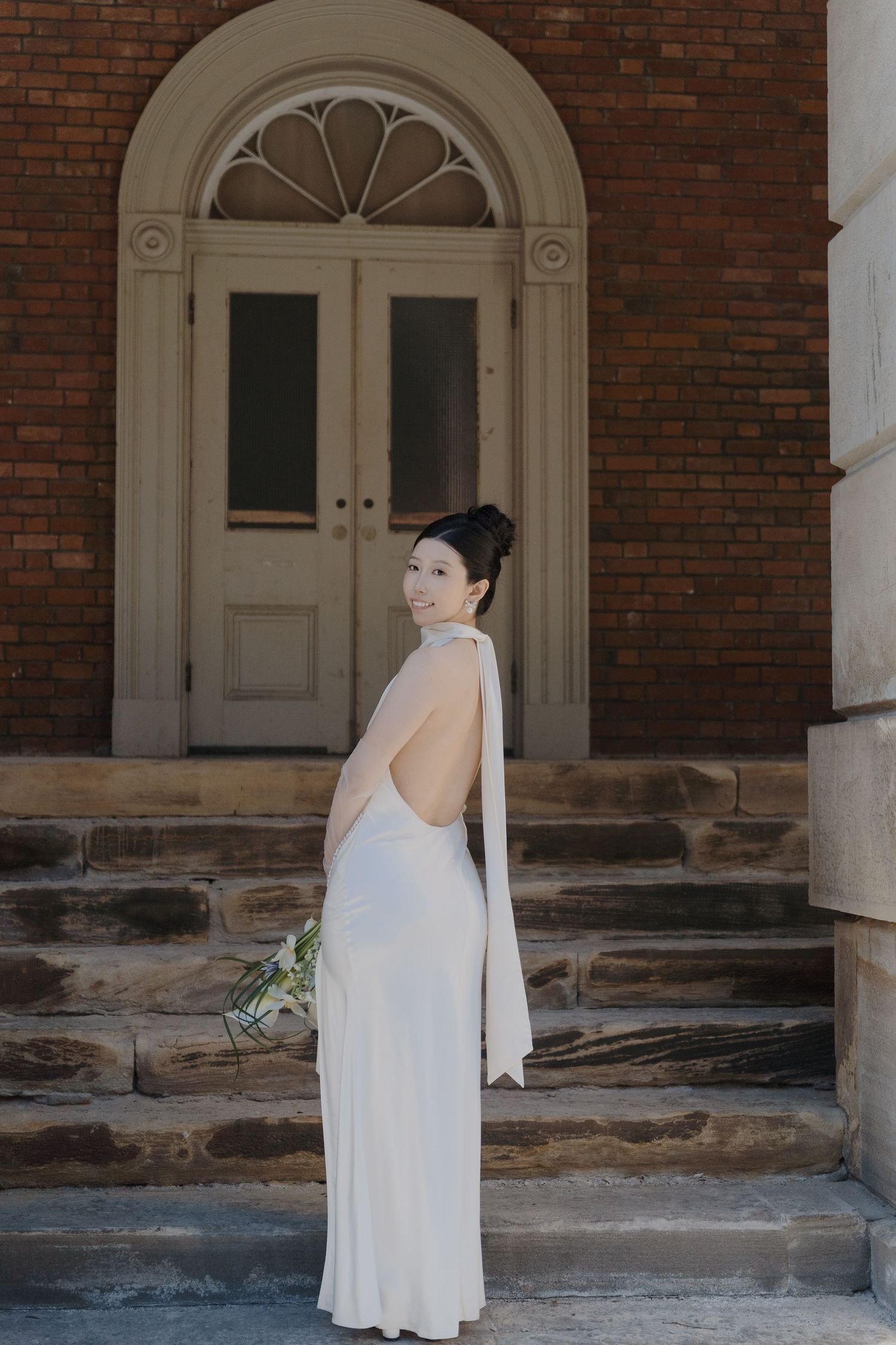Bride in backless gown holding bouquet on Osgoode Hall stone steps for editorial Toronto City Hall wedding photography.