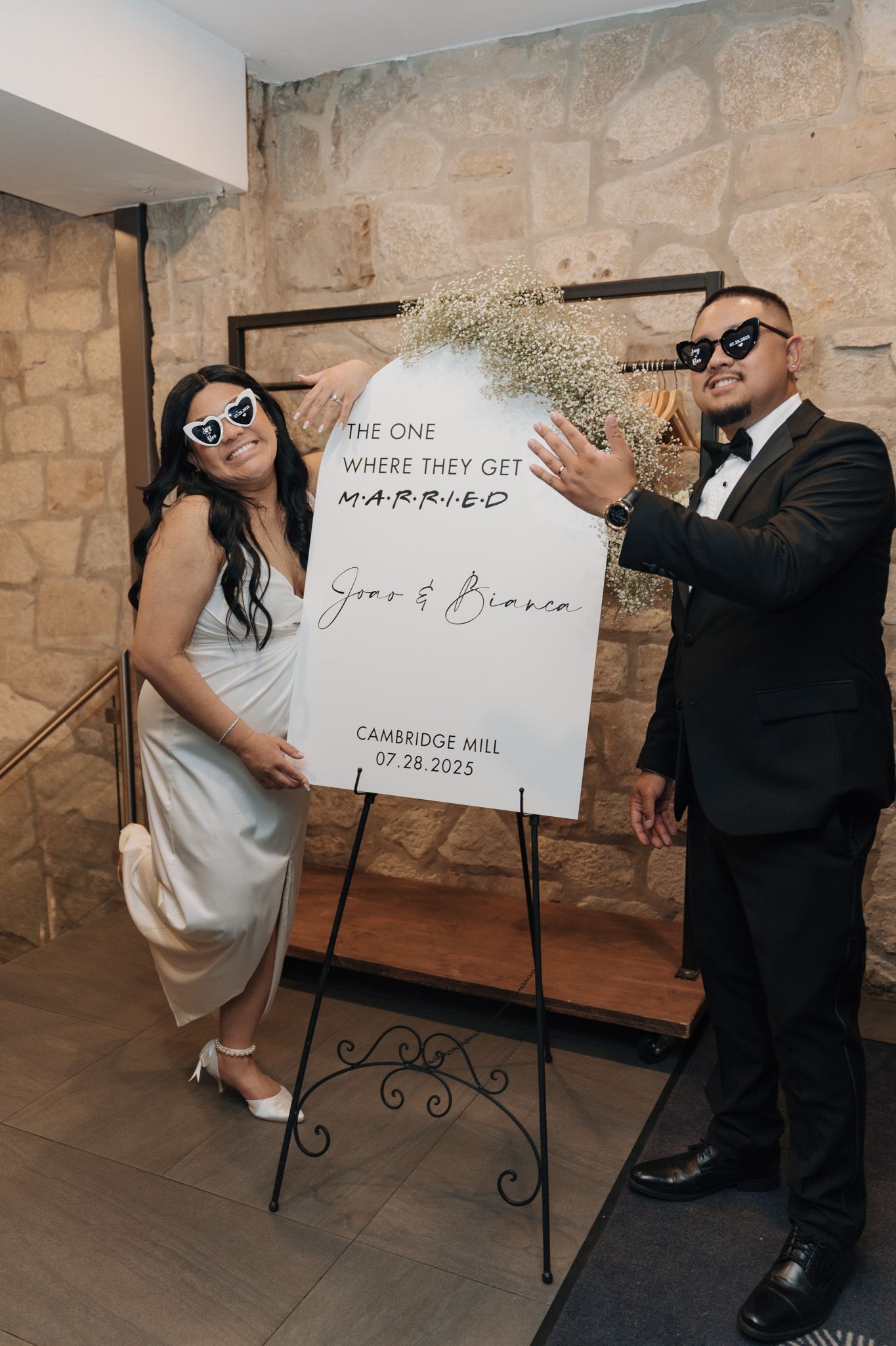 Couple posing beside a Friends-themed welcome sign at Cambridge Mill in Cambridge, Ontario during their wedding celebration.