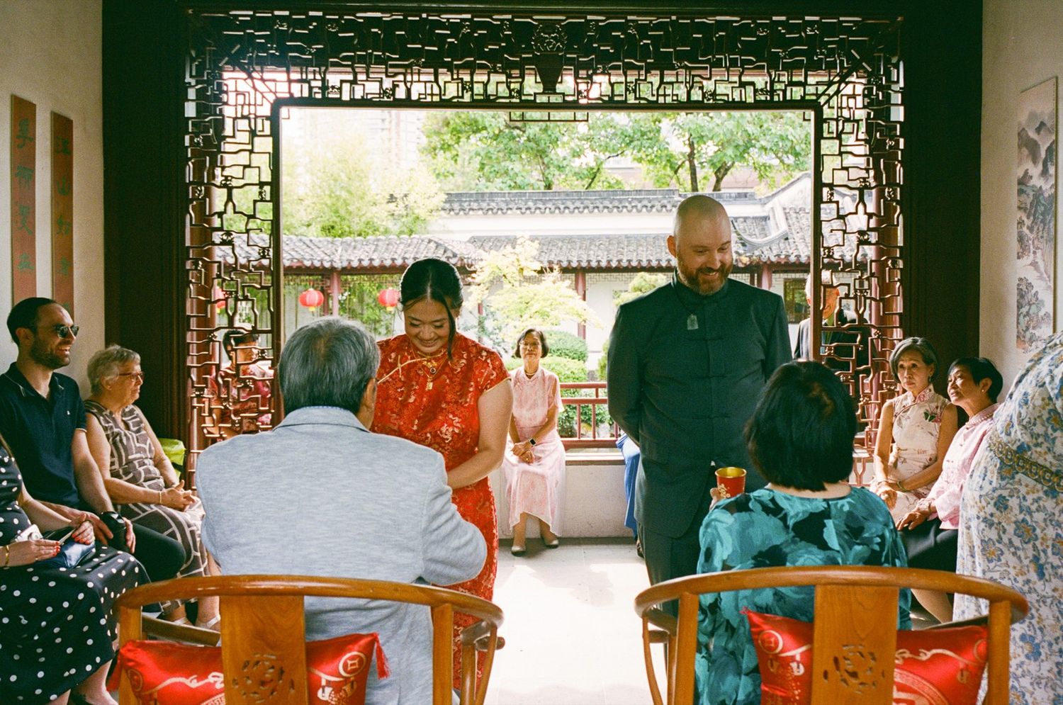 Couple in traditional Chinese attire during an intimate wedding ceremony in a classical garden pavilion with seated guests.