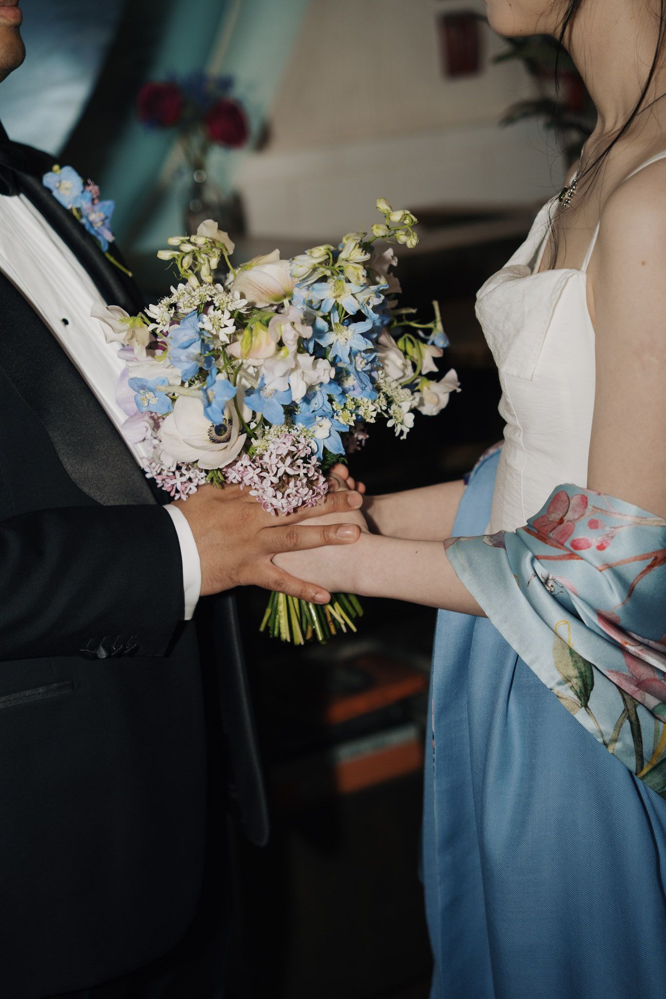 Bride and groom holding hands with a blue and white wedding bouquet during a ceremony.