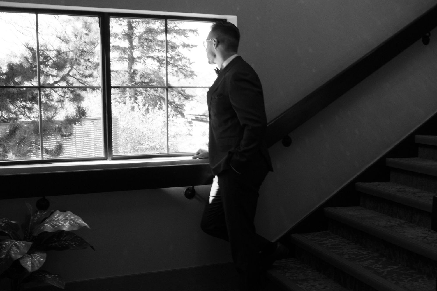 Black and white groom looking out a window by a staircase at The Manor in King City during his Jewish wedding morning.