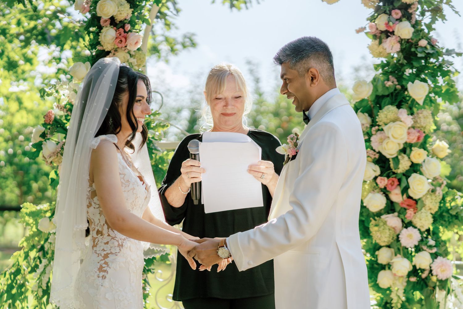 Couple exchanging vows beneath a peach rose floral arch at Kurtz Orchards in Niagara-on-the-Lake outdoor wedding ceremony.
