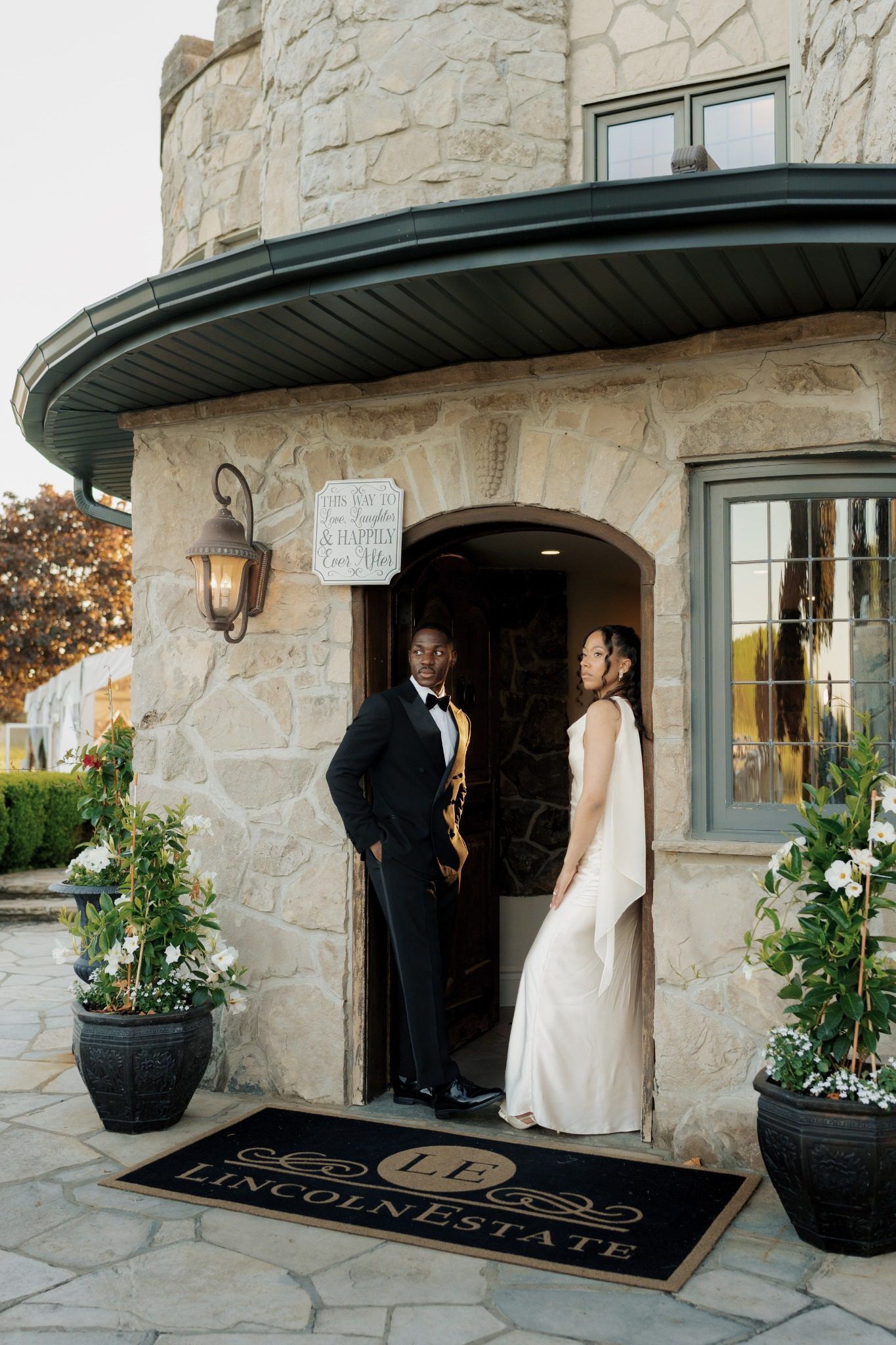 Couple in wedding attire posing at the arched entrance of Lincoln Estate venue, surrounded by floral arrangements.