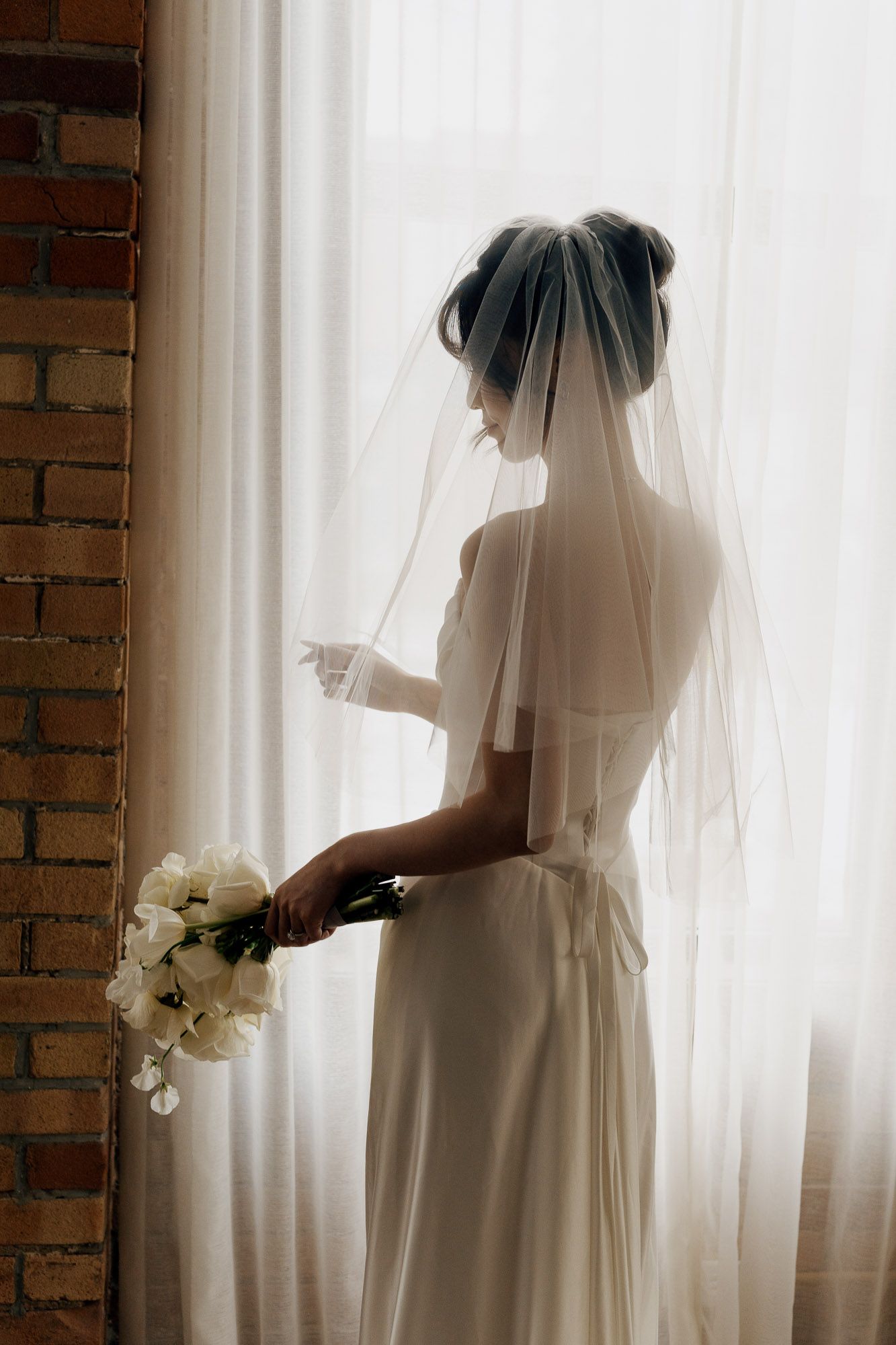 Bride in white gown and veil holding tulip bouquet by a sunlit window at Archive Studio in Toronto for intimate wedding photography.