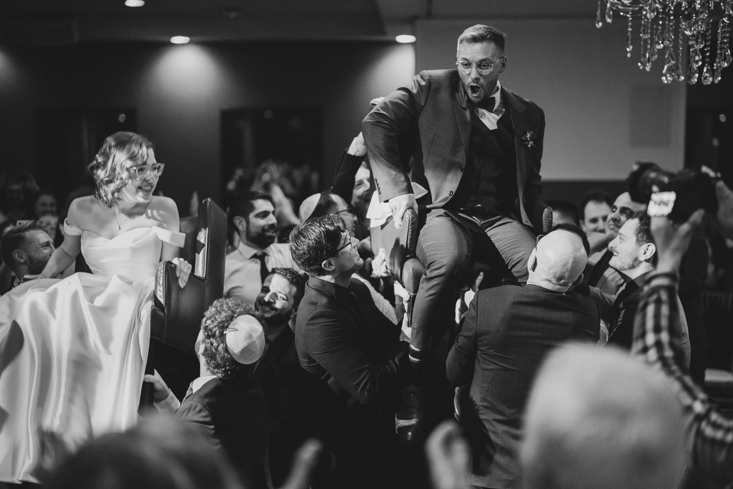 Black and white groom lifted by guests during the hora at The Manor in King City for lively Jewish wedding photography.