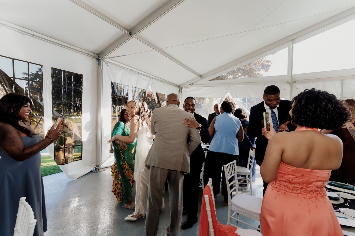 Guests mingling under a white tent at an elegant outdoor wedding reception celebration.