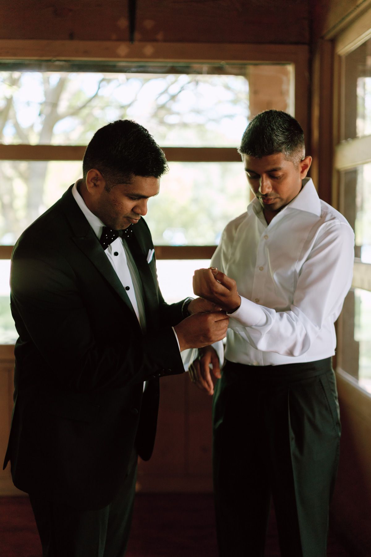 Groom having cufflinks fastened by groomsman in a rustic room at Kurtz Orchards in Niagara-on-the-Lake wedding morning.