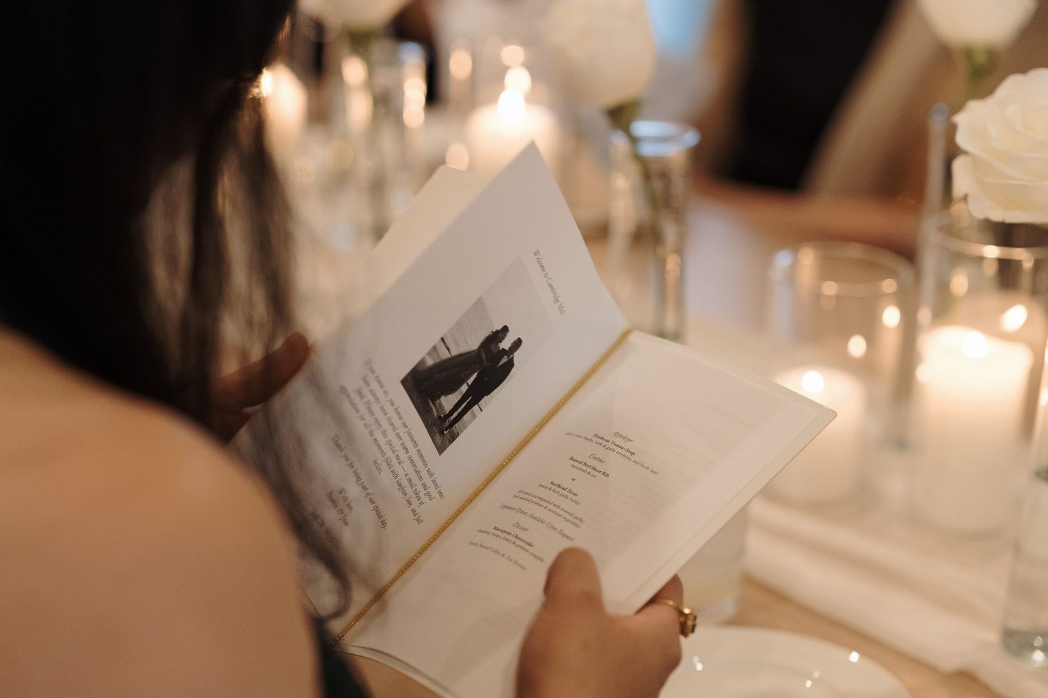 Guest reading a wedding program at a candlelit reception table at Cambridge Mill in Cambridge, Ontario for candid wedding photography.
