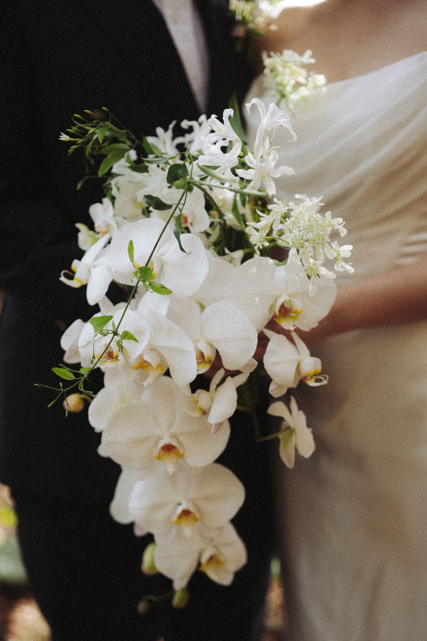 Bride holding a cascading white orchid bouquet against her ivory gown at Razi Estate in Schomberg for cinematic forest wedding photography.