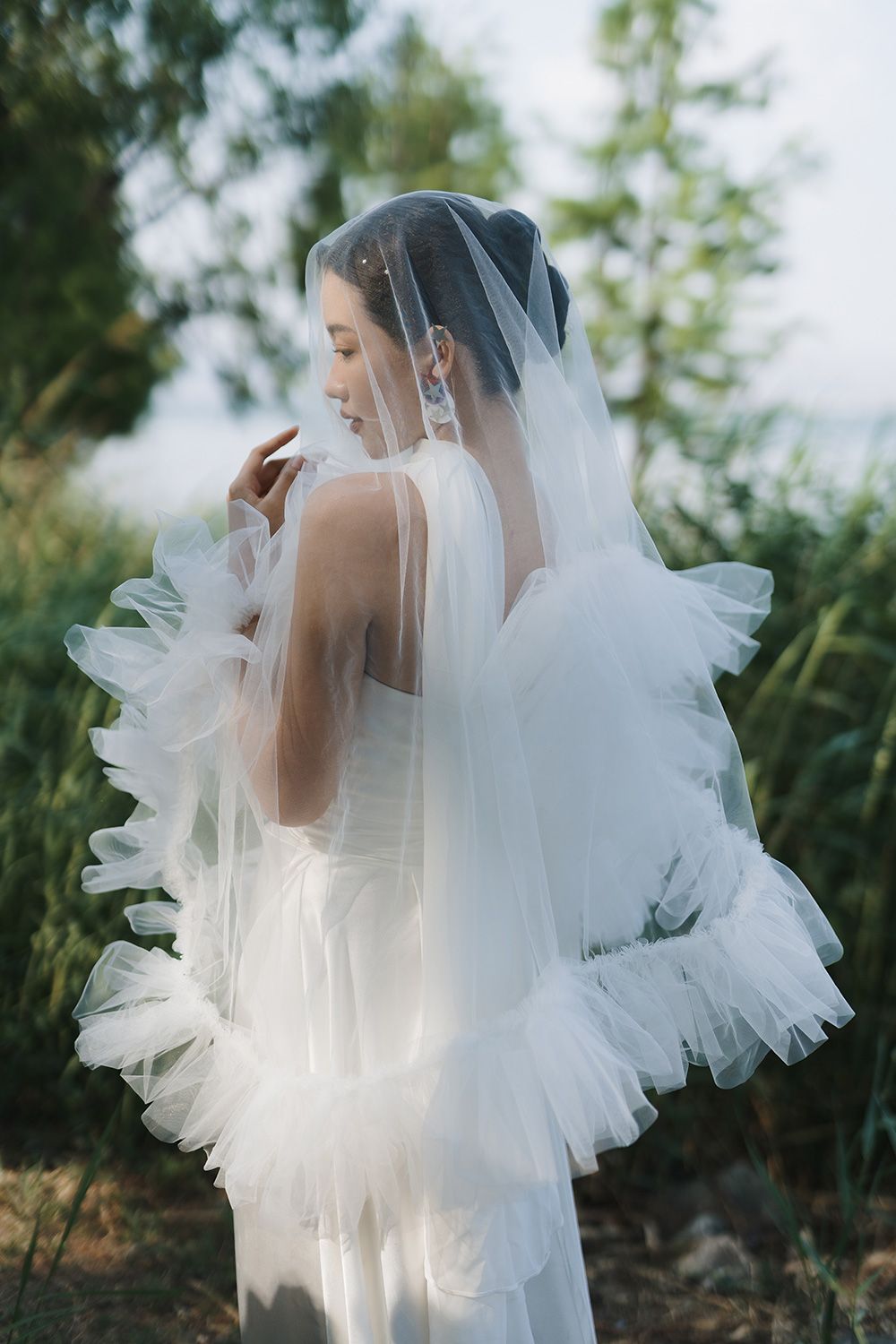 Elegant Bride in a ruffled veil posing among lush greenery during a Vancouver bridal portrait session for editorial wedding photography