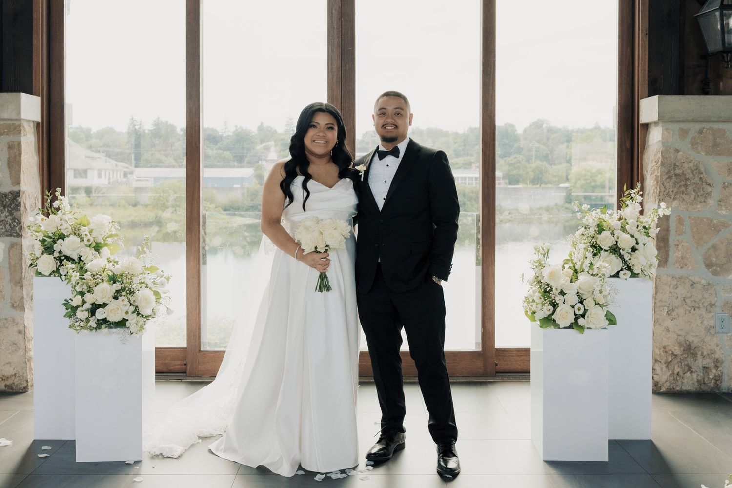 Bride and groom standing with white florals at Cambridge Mill in Cambridge, Ontario during their elegant wedding ceremony.