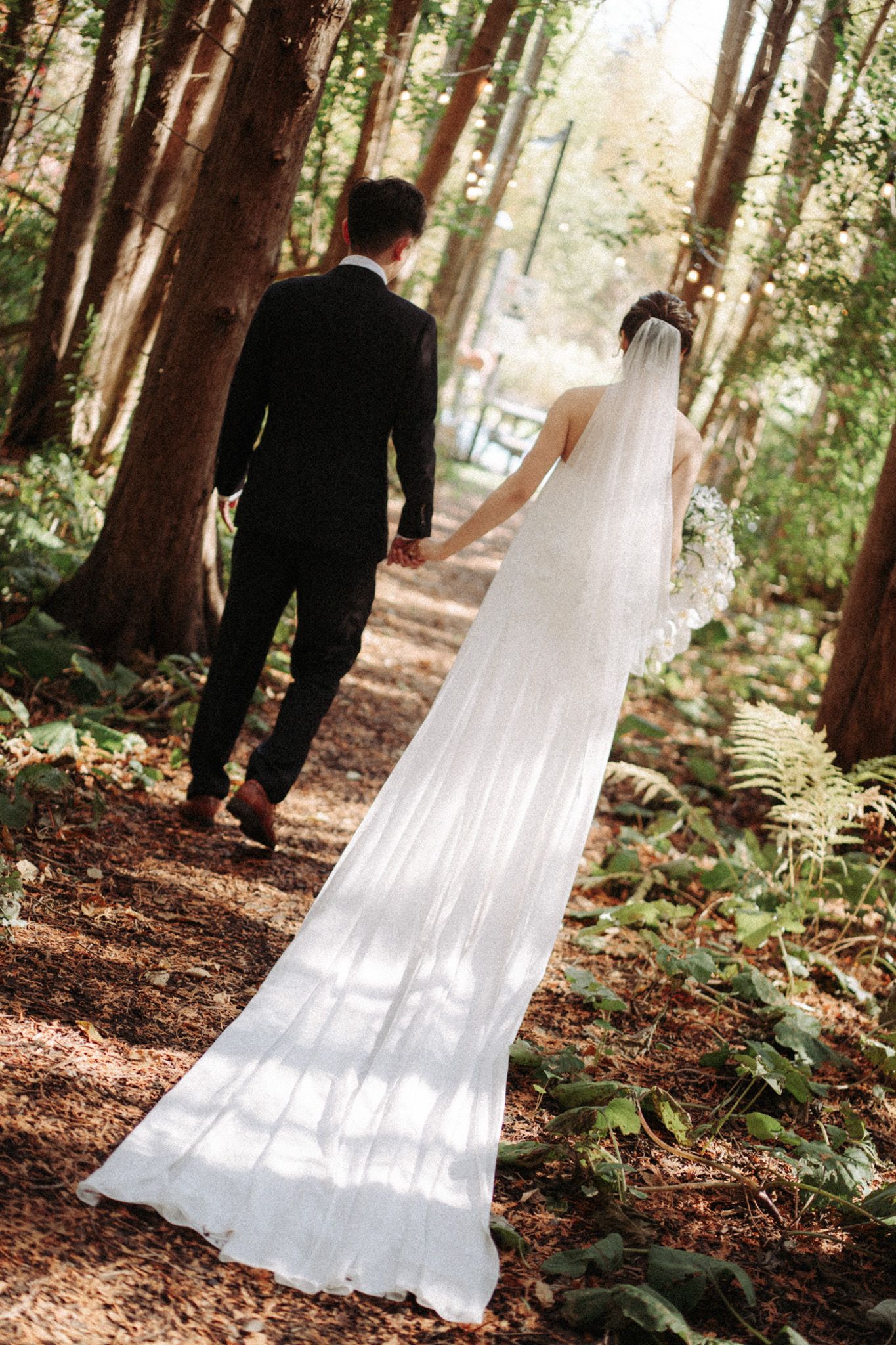 Bride and groom walking hand in hand through a sunlit forest path at Razi Estate in Schomberg for forest wedding photography.