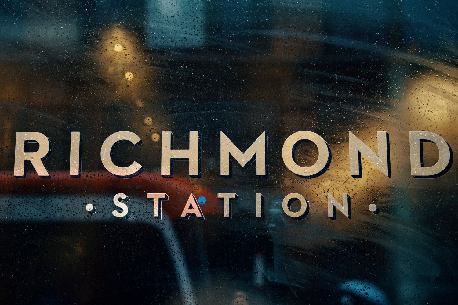 Richmond Station restaurant logo displayed on a rain-speckled window with warm bokeh lights in the background.