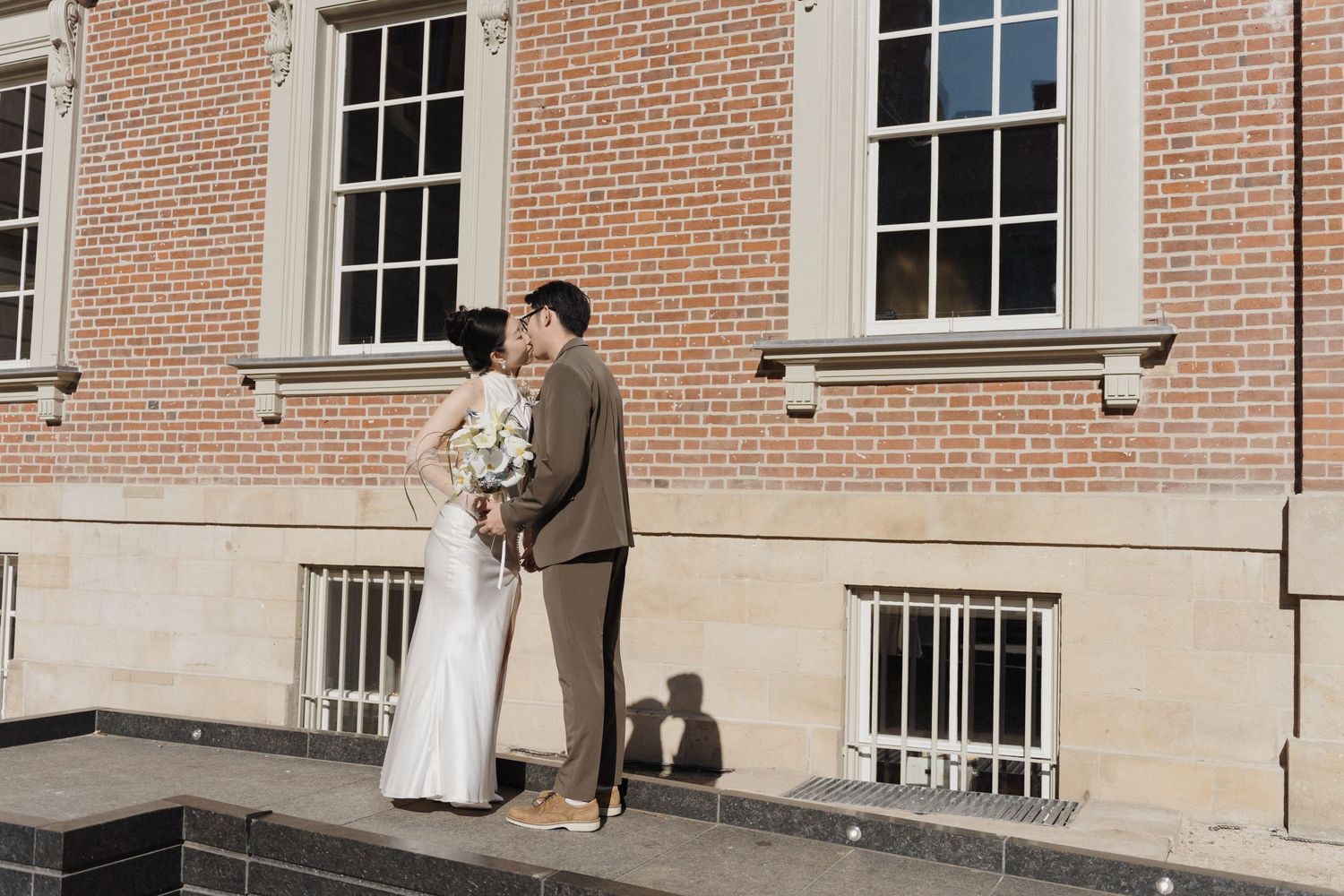 Bride and groom kissing outside Osgoode Hall’s heritage building with white bouquet for timeless Toronto City Hall wedding photography.