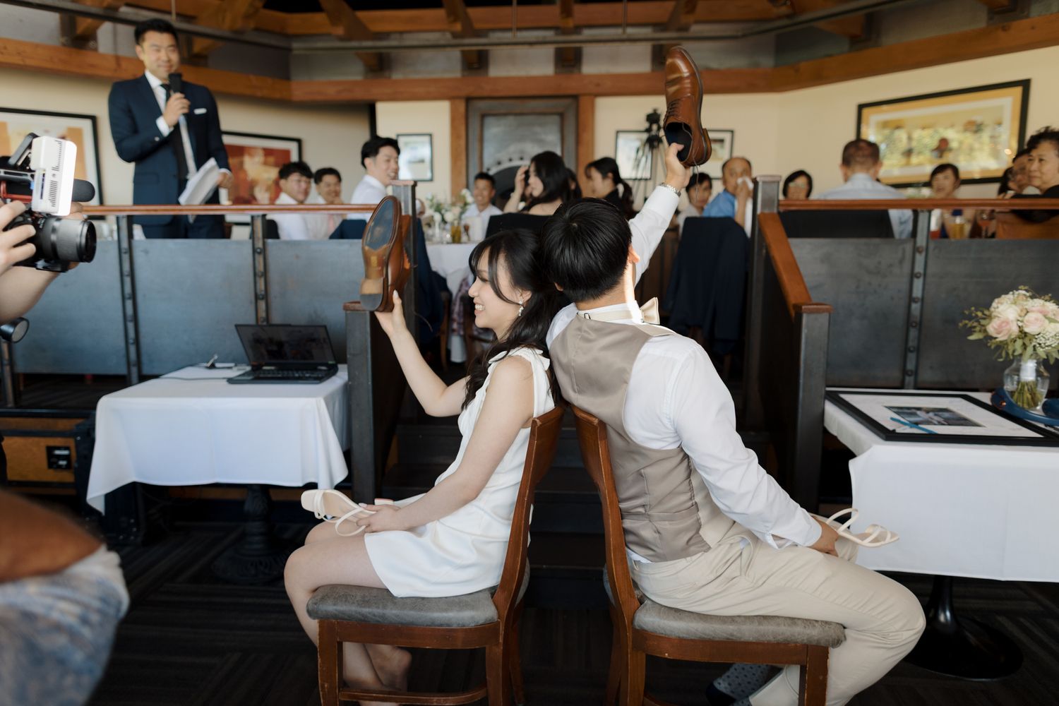 Bride and groom sit back-to-back during a fun wedding reception game while guests watch and cheer.