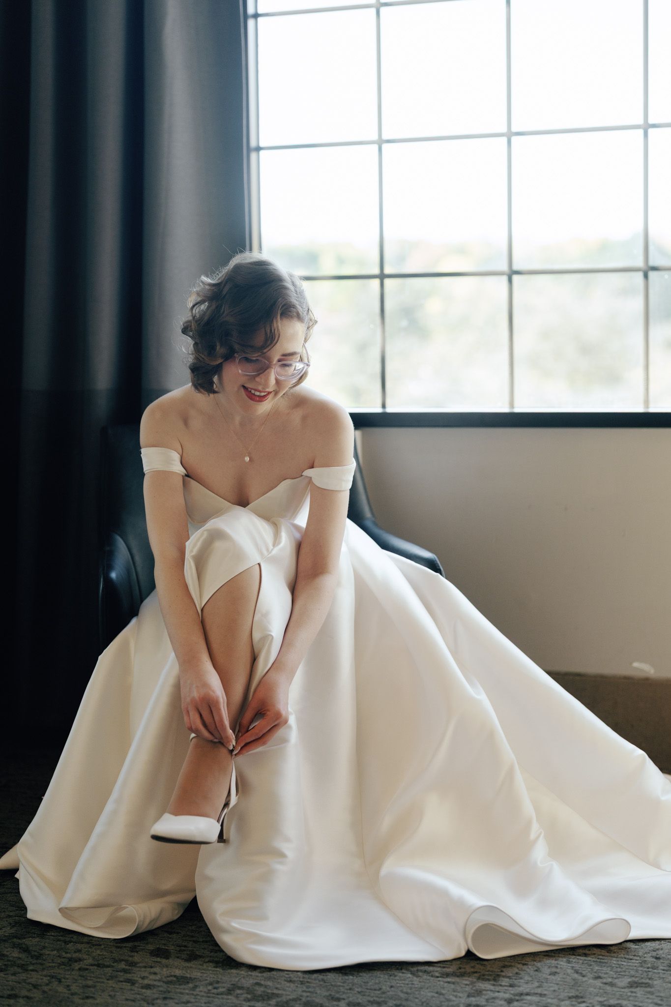 Bride fastening her wedding shoe by a window at The Manor in King City during her Jewish wedding morning preparations.