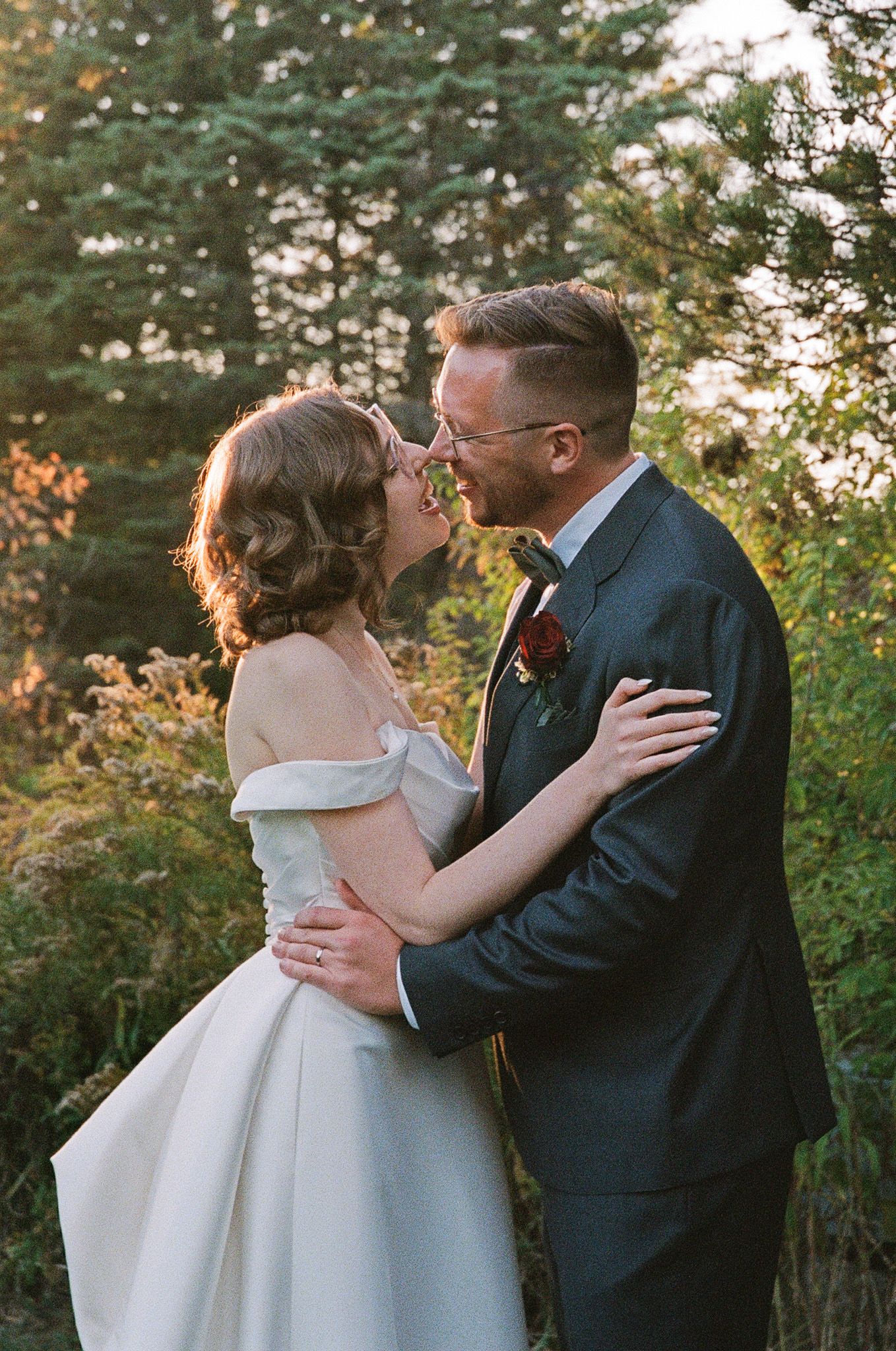 Bride and groom leaning in for a kiss among lush greenery at The Manor in King City during their Jewish wedding portraits.