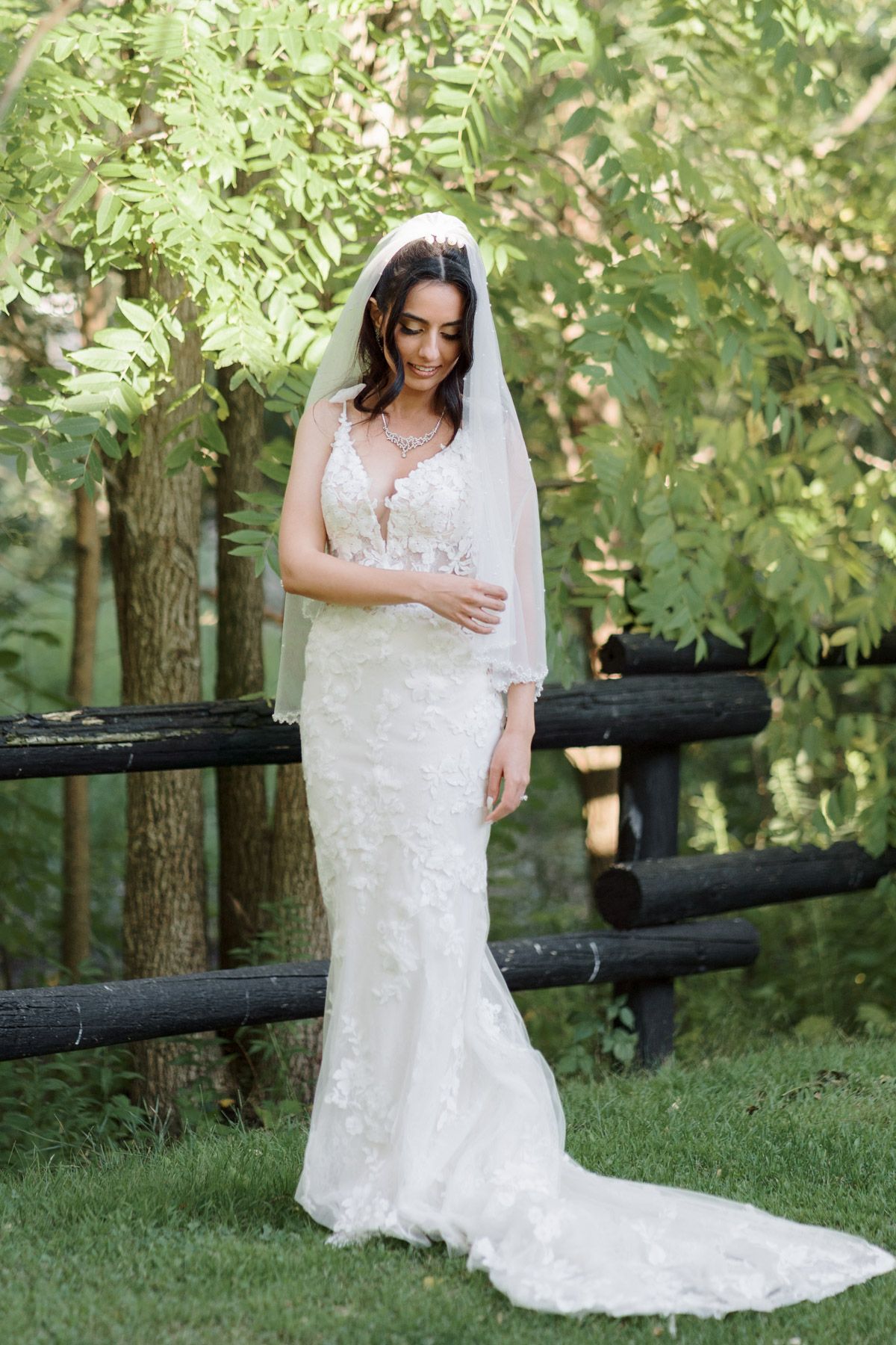 Bride in a lace mermaid gown and veil posing by a rustic wooden fence at Kurtz Orchards in Niagara-on-the-Lake wedding portraits.