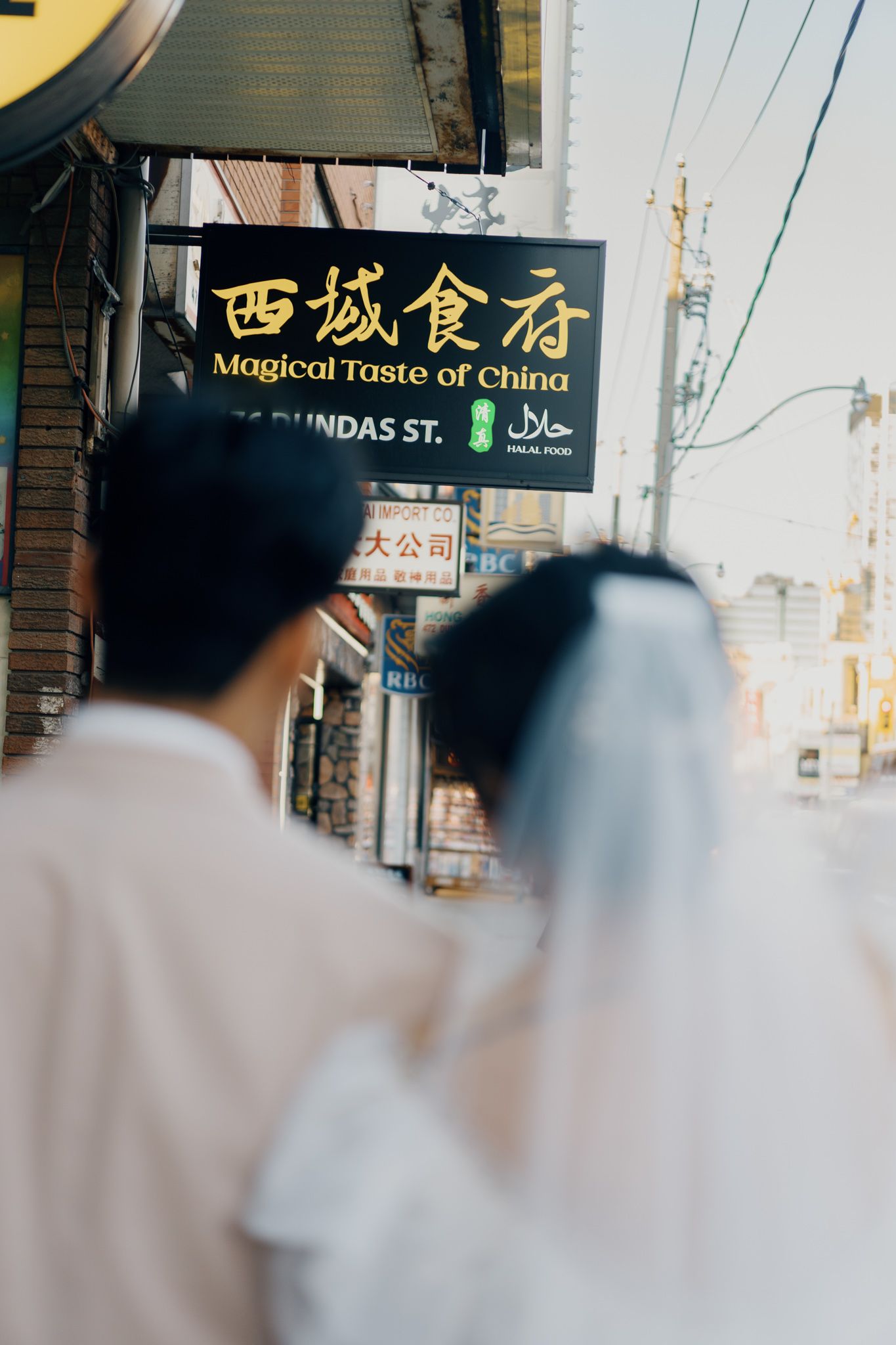 Couple walking toward Magical Taste of China on Dundas Street in Toronto Chinatown during an 80s Hong Kong-inspired pre-wedding shoot