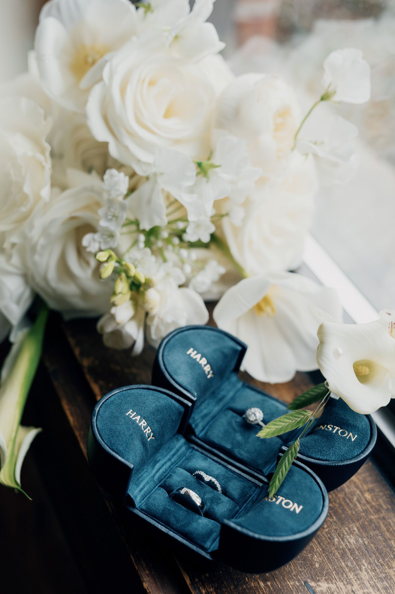 Harry Winston wedding rings in a blue velvet box beside white roses at Archive Studio in Toronto for editorial wedding photography