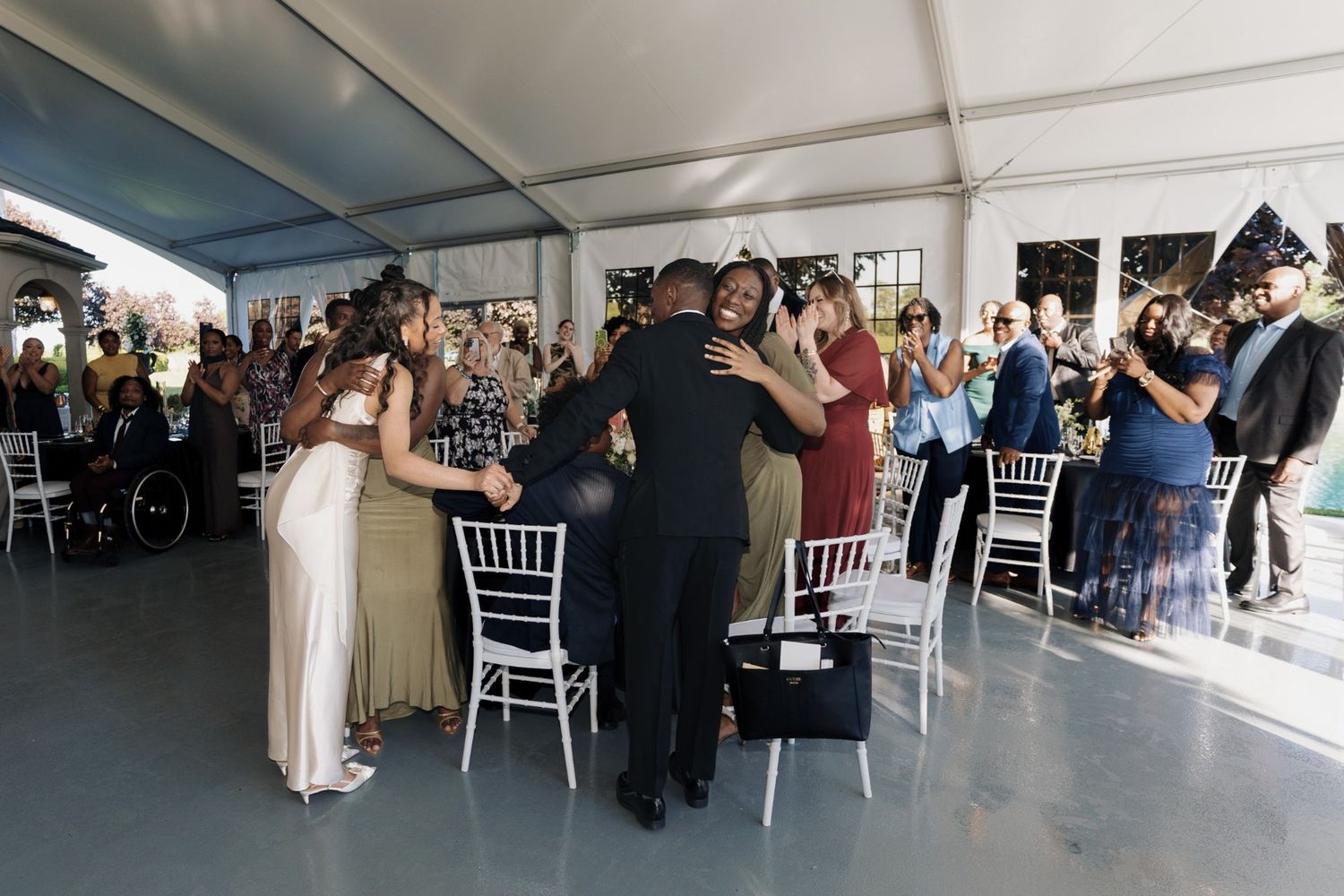 Guests dancing and celebrating at an elegant wedding reception under a white tent with chiavari chairs.
