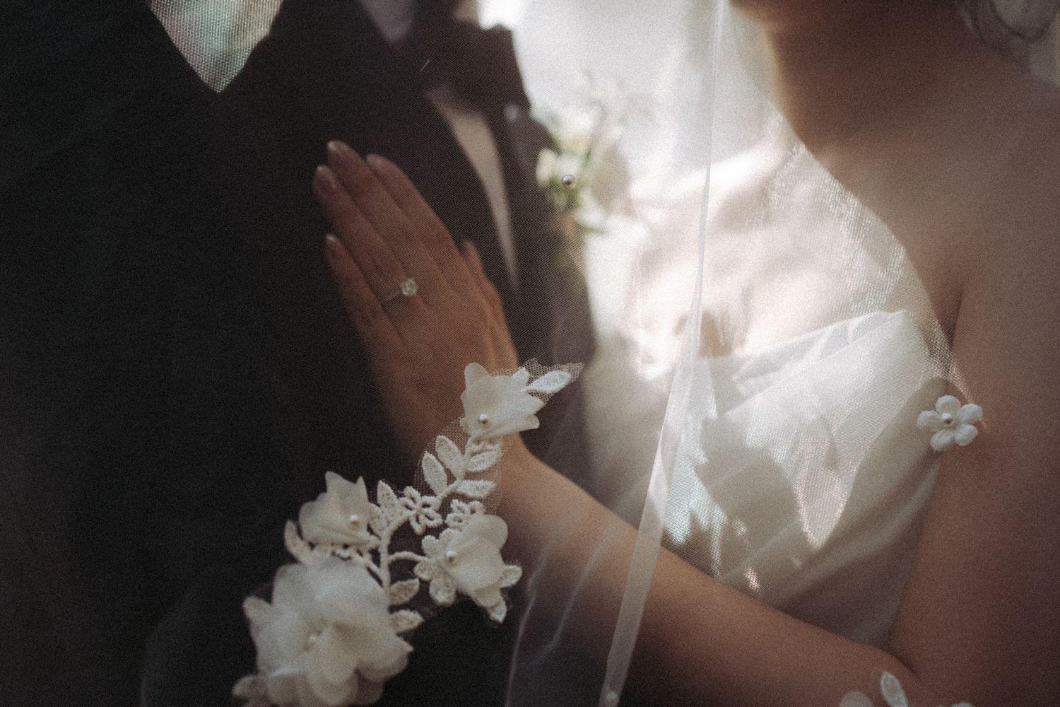 Bride and groom holding hands under a floral veil, showing diamond ring at Razi Estate in Schomberg for cinematic wedding photography.