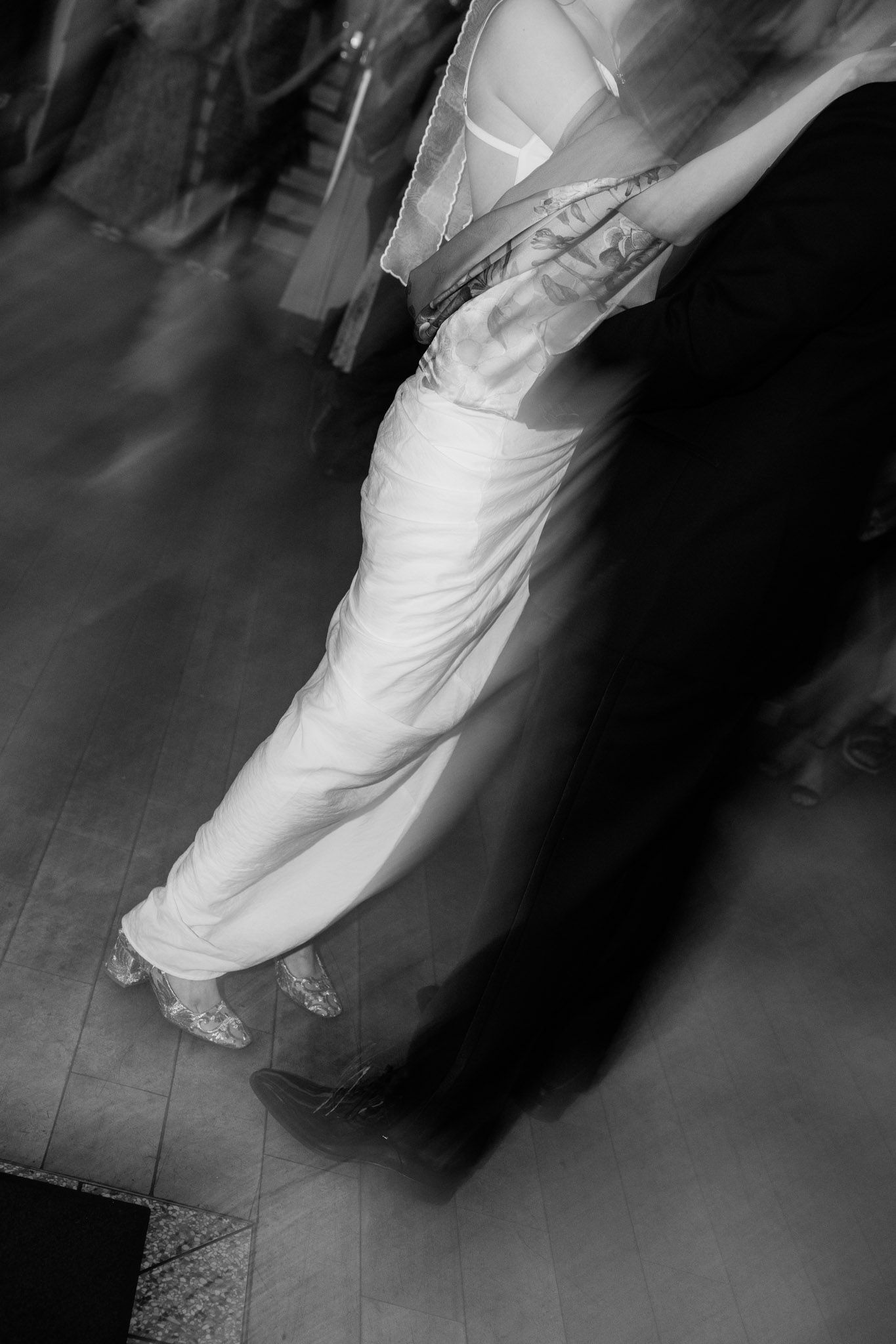 Black and white motion blur photo of couple dancing, woman in white gown and man in dark suit on dance floor.