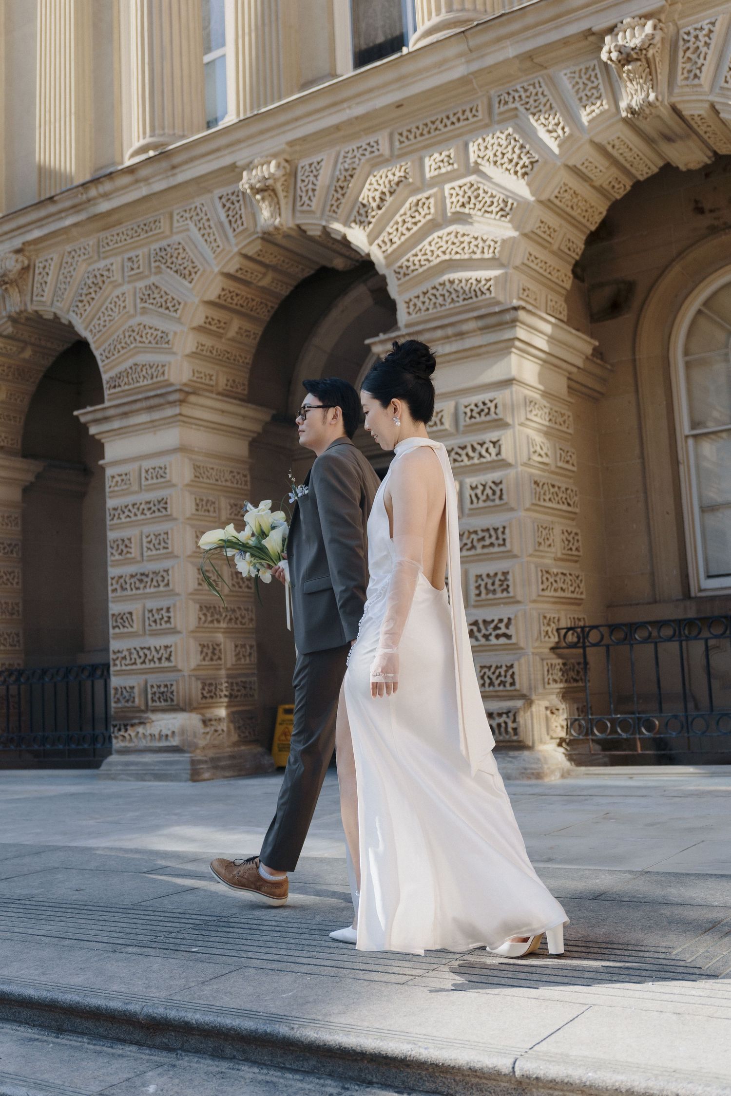 Bride and groom walking past Osgoode Hall’s vintage stone architecture for editorial Toronto City Hall wedding photography.