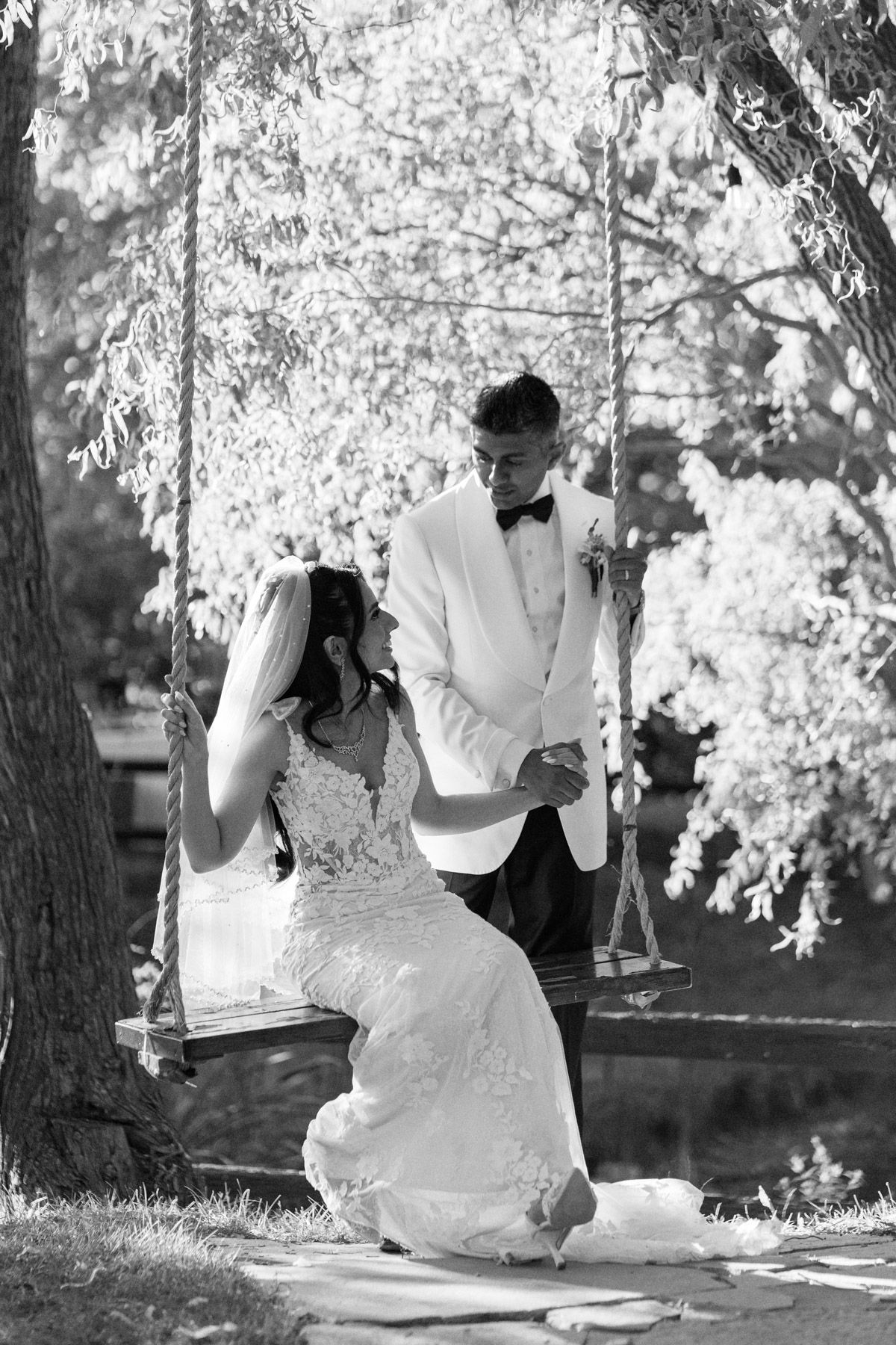 Black and white bride on a tree swing holding groom’s hand at Kurtz Orchards in Niagara-on-the-Lake wedding portraits.