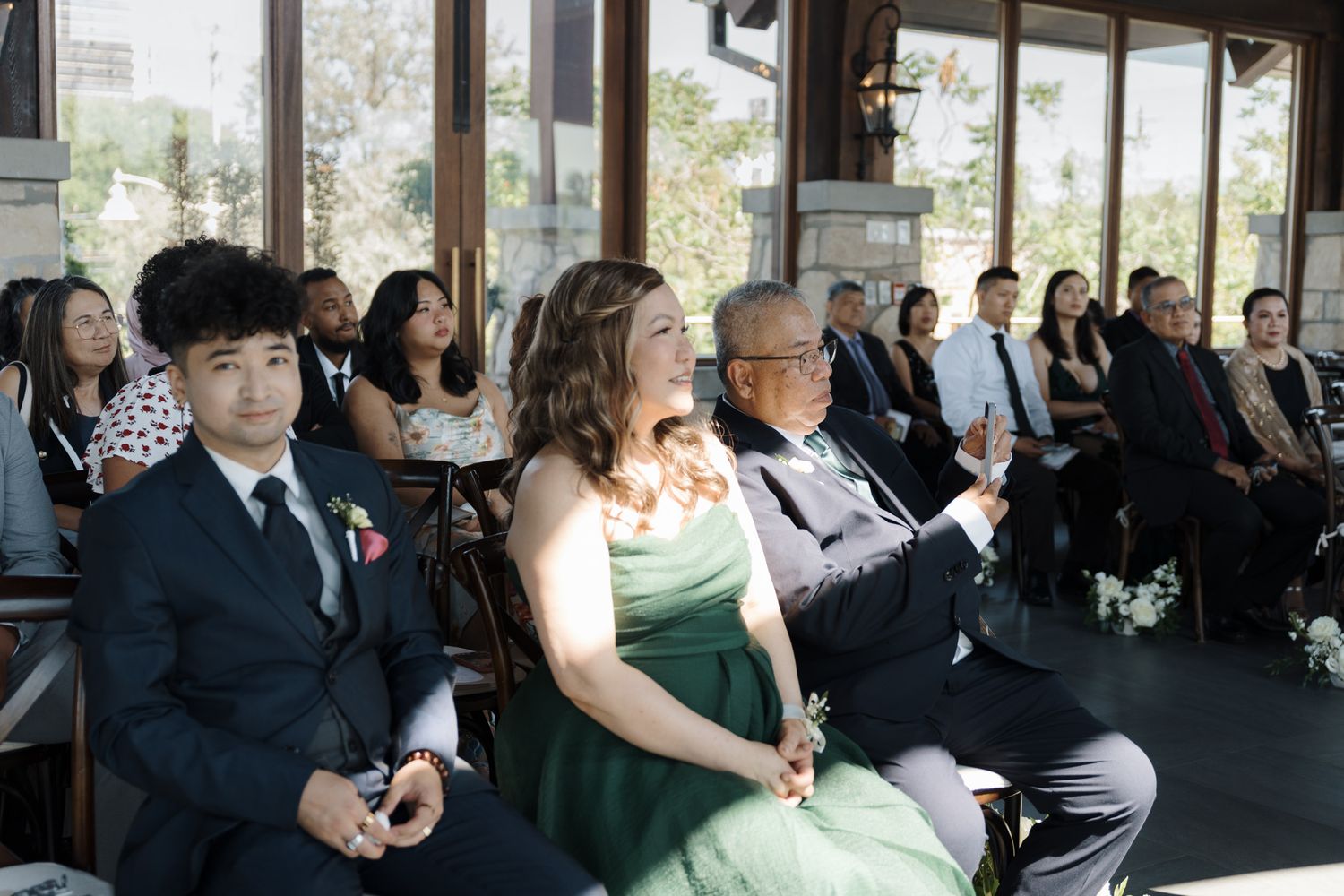 Wedding guests seated in a sunlit ceremony venue at Cambridge Mill in Cambridge, Ontario for candid wedding photography.