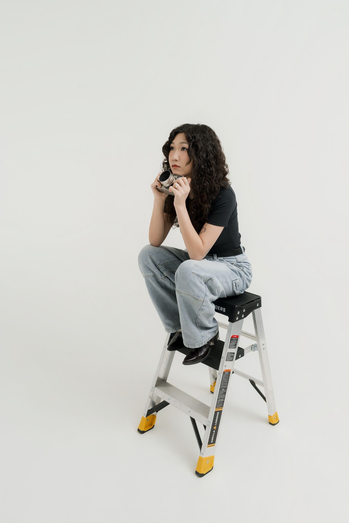 Studio founder Clarise Xia posing on a step ladder during a clean studio branding day portrait session.