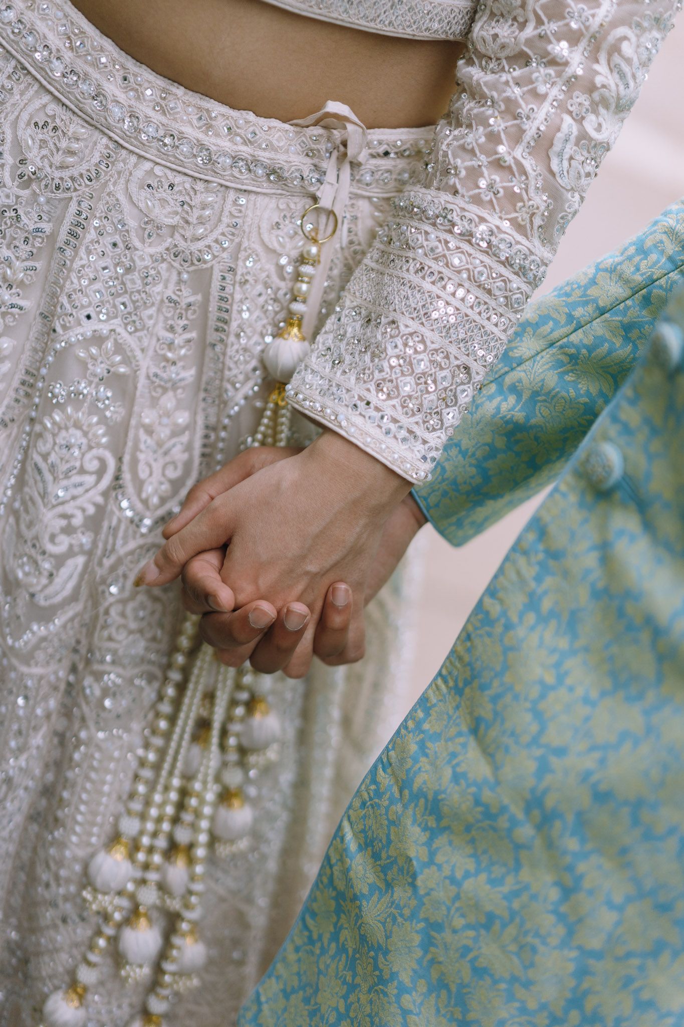 Couple holding hands in traditional South Asian attire, featuring white embroidered lehenga. McMasters University, Hamilton Ontario.