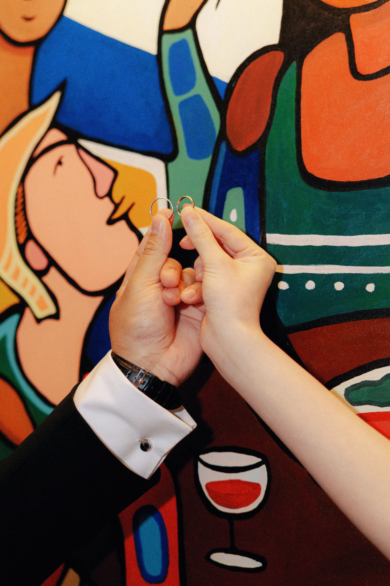 Couple exchanging wedding rings in front of a colorful pop art painting at their ceremony.