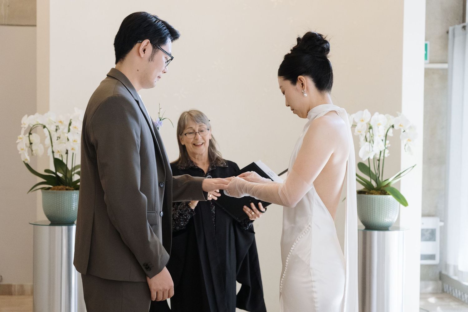 Couple exchanging rings with officiant and white orchids during an intimate Toronto City Hall civil ceremony.
