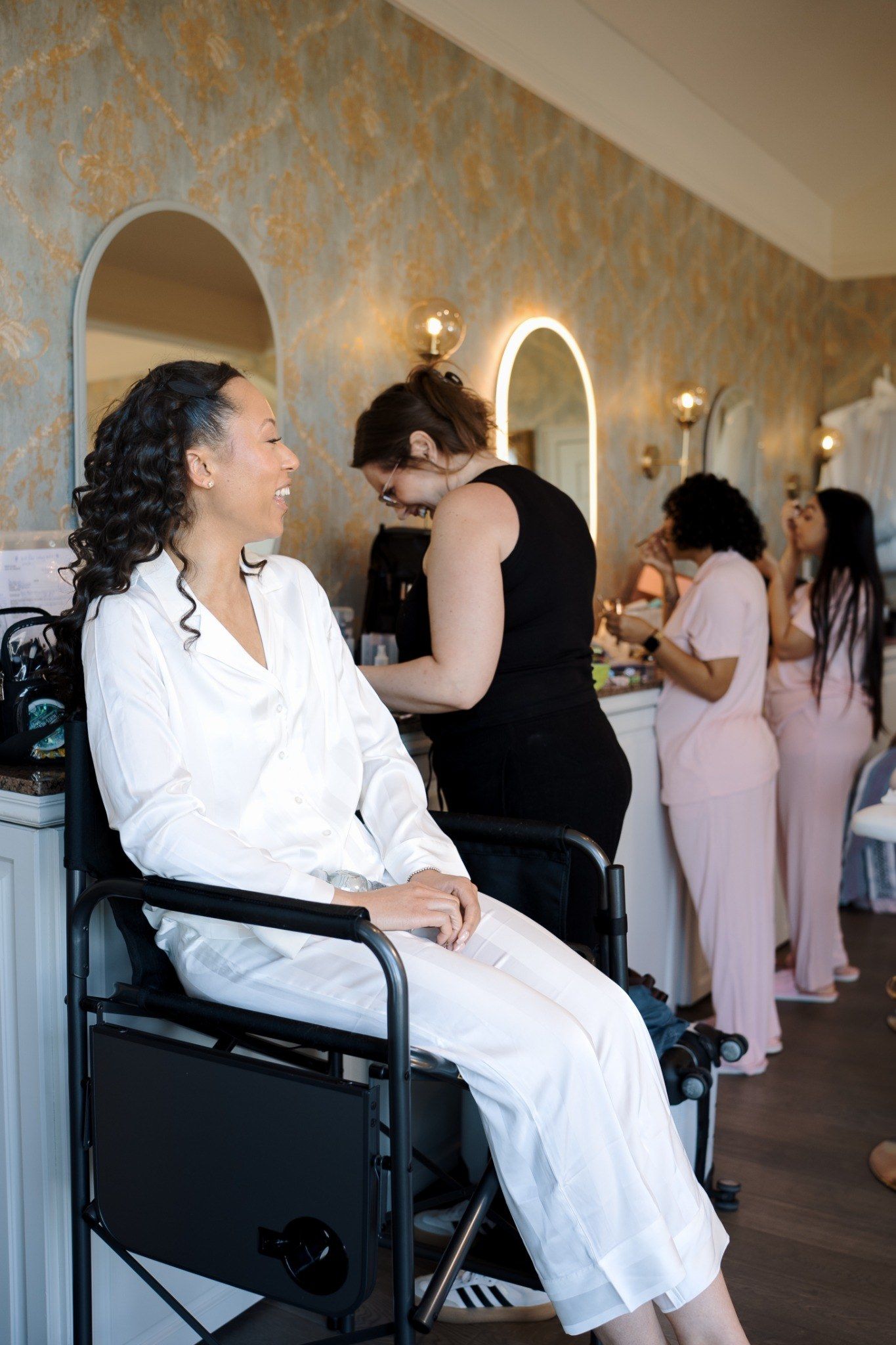 Bride in white satin robe smiling in salon chair during wedding morning preparations.