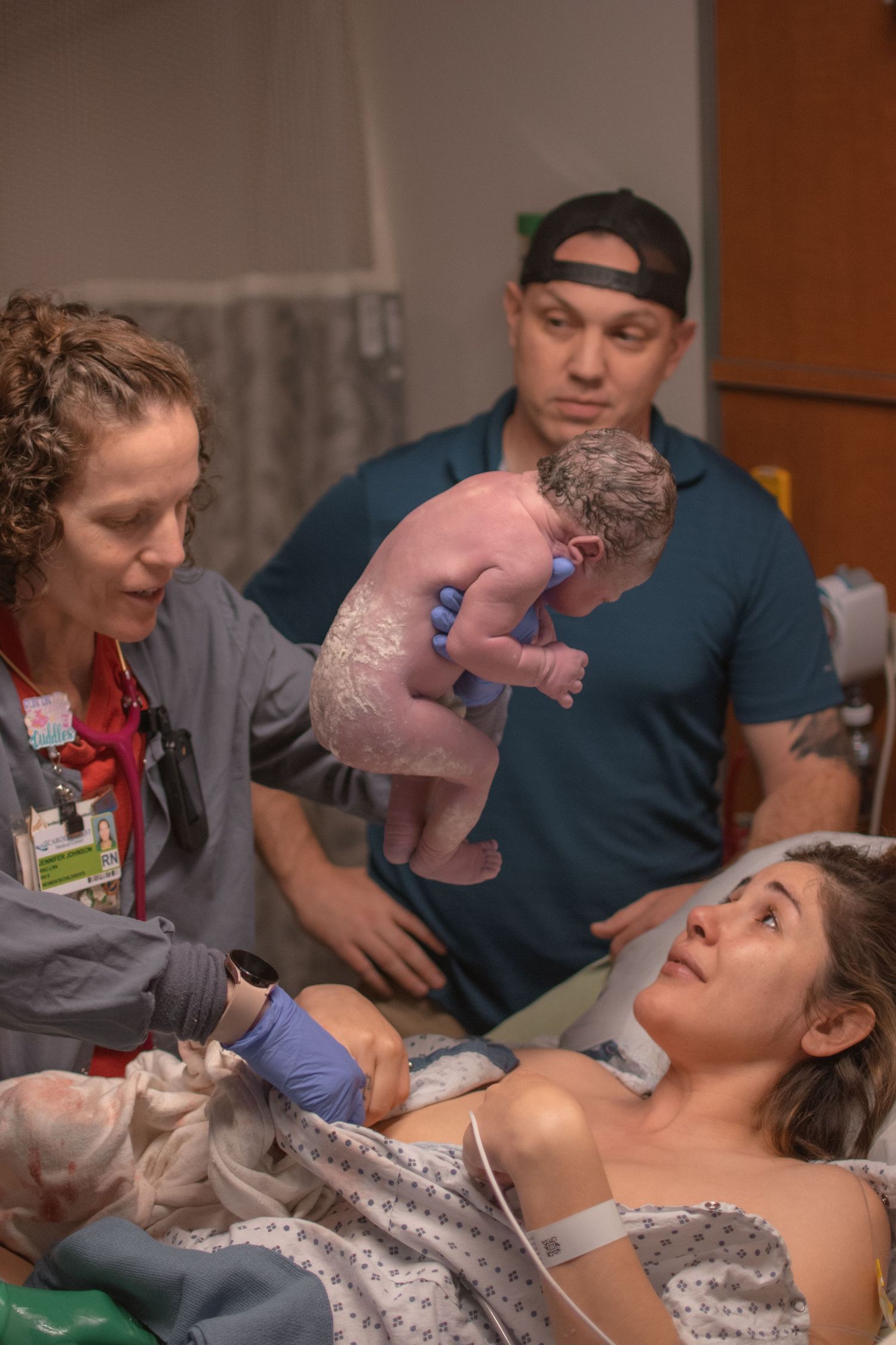 A nurse holds a newborn baby moments after birth while parents look on in a hospital delivery room.