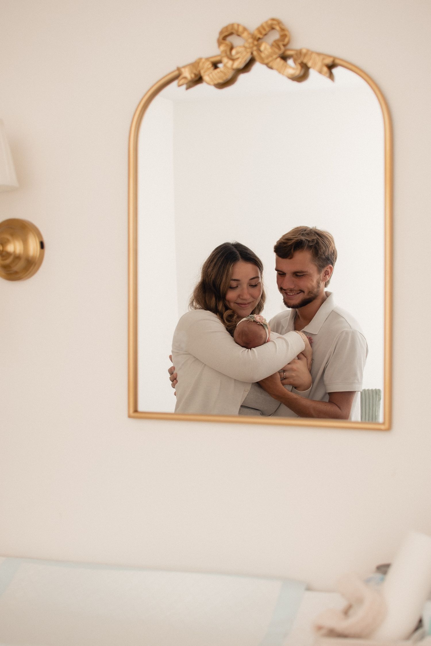 Couple embracing and smiling together, reflected in an ornate gold arch mirror on a white wall.
