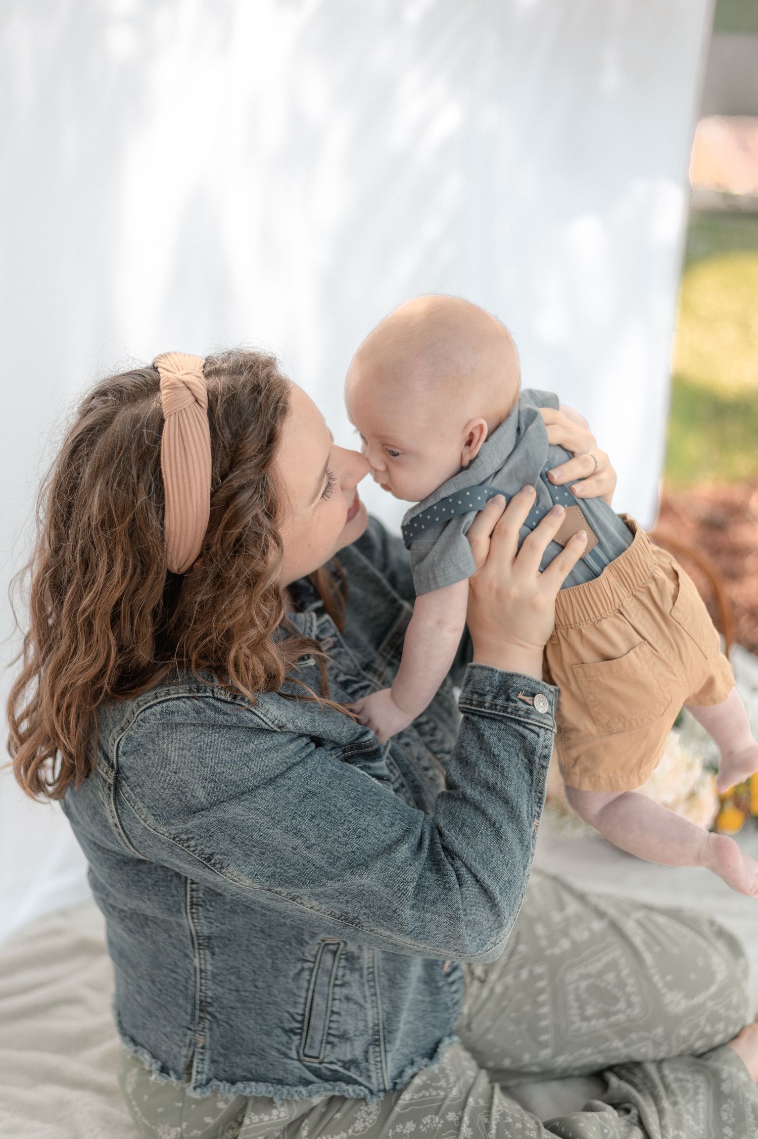 A mother holds her baby up to her face for a sweet nose-to-nose moment outdoors.