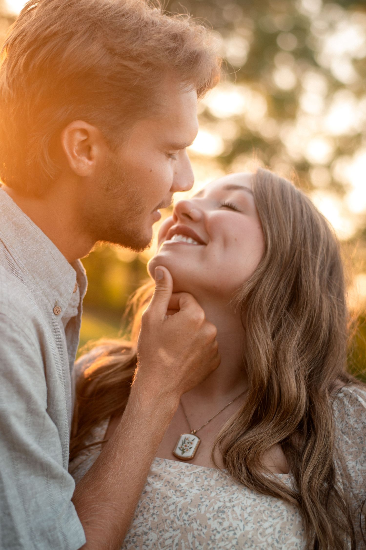 A couple shares a romantic moment at golden hour, with the man leaning in to kiss the smiling woman outdoors.