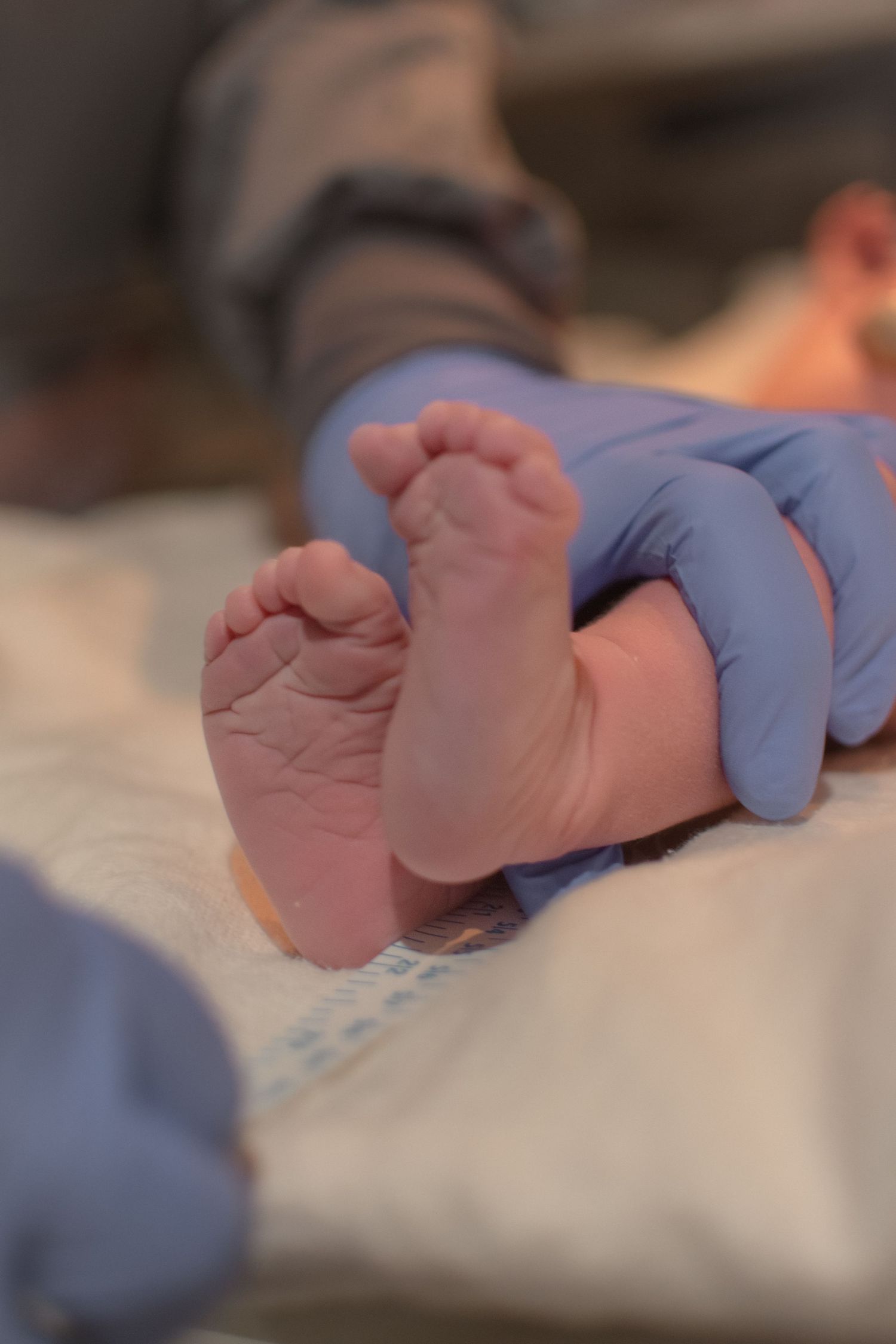 Close-up of newborn baby tiny feet held by gloved medical professional hands after birth.