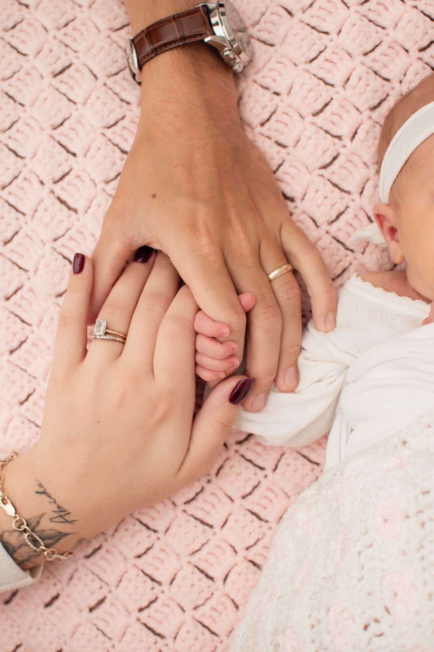 Parents and newborn baby holding hands together on a pink knitted blanket, symbolizing family love and new beginnings.
