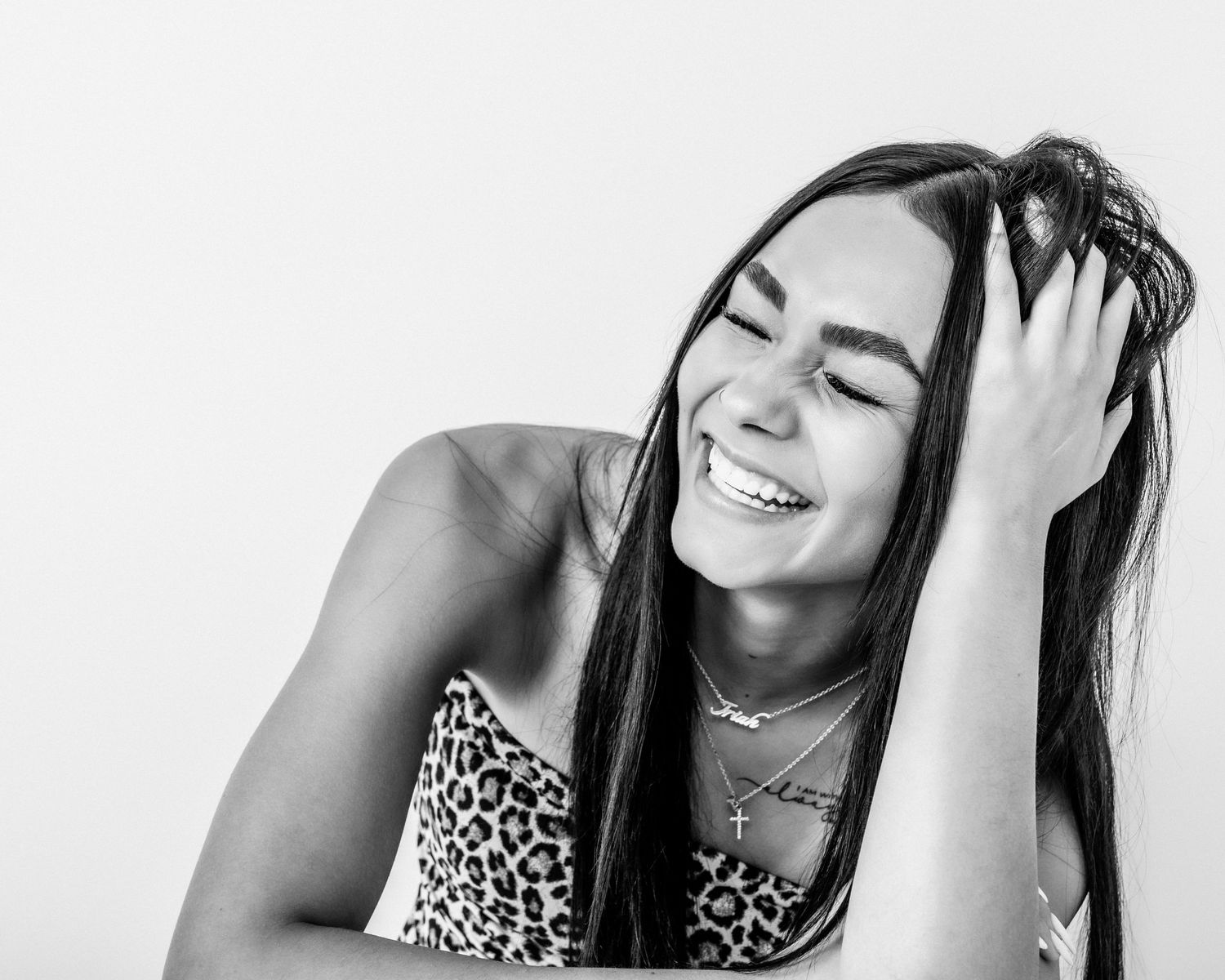 Black and white portrait of a young woman laughing with her hand in her long dark hair.