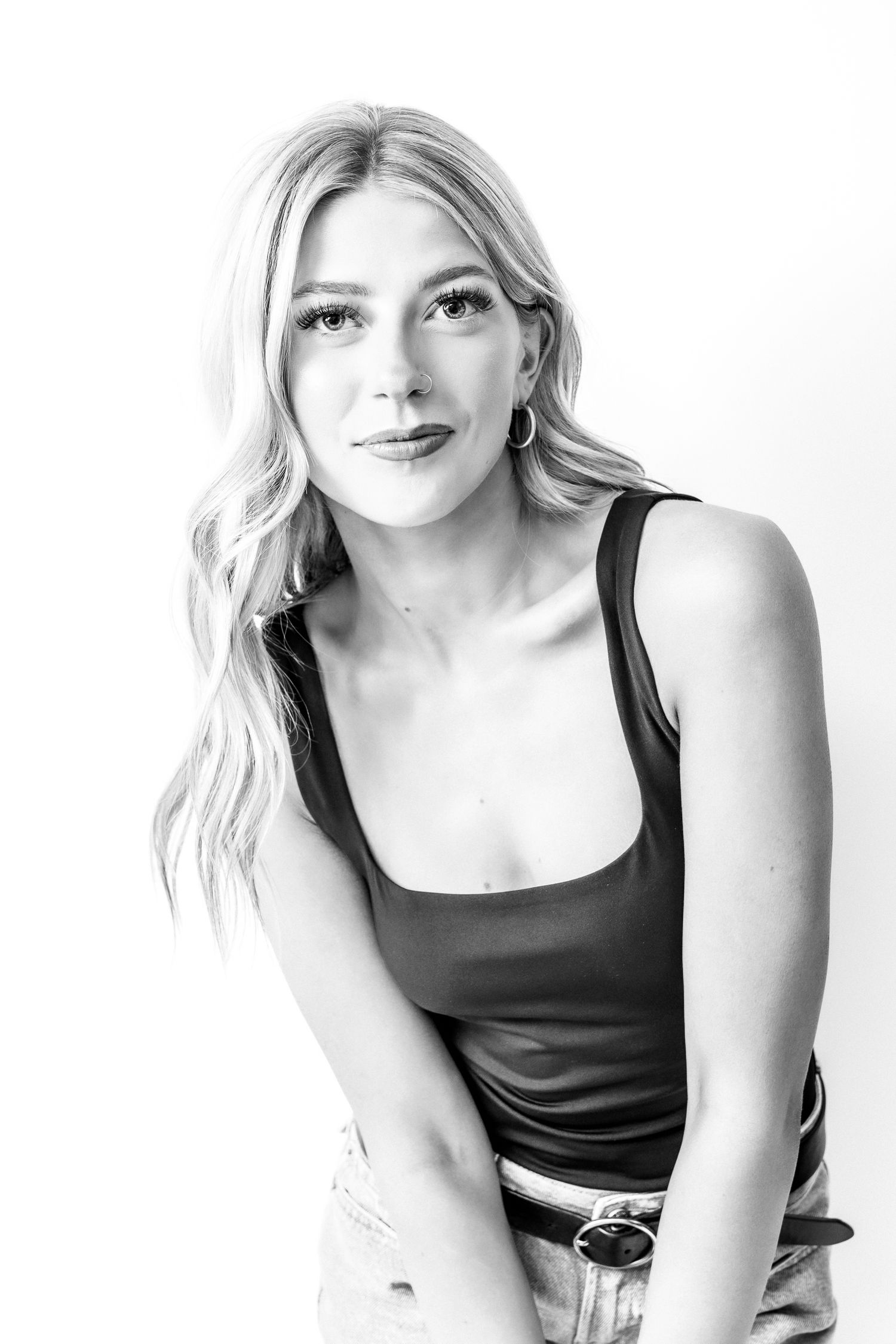 Black and white portrait of a young blonde woman in a tank top, posing confidently against a white background.