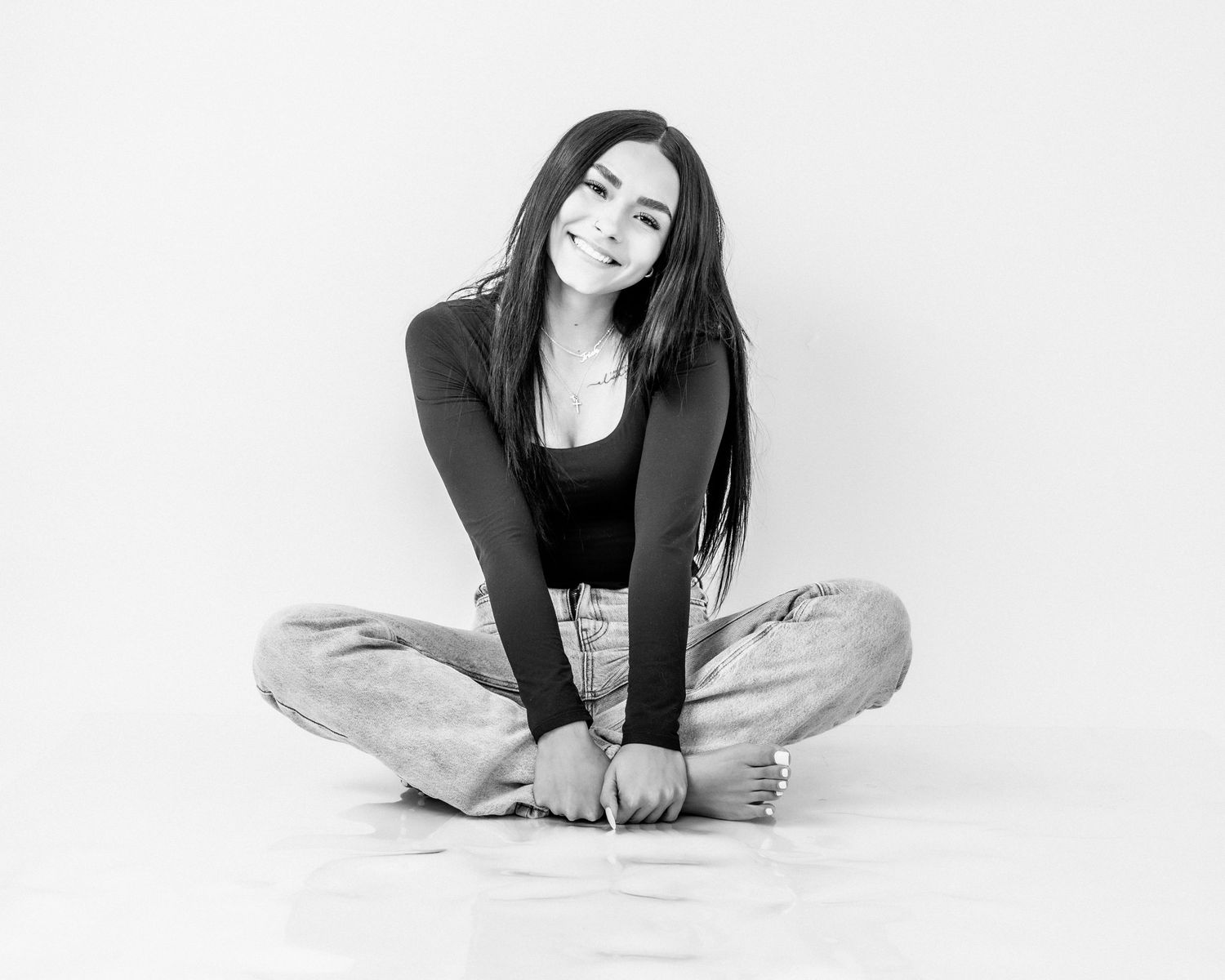 Black and white photo of a young woman with long dark hair sitting cross-legged on the floor.