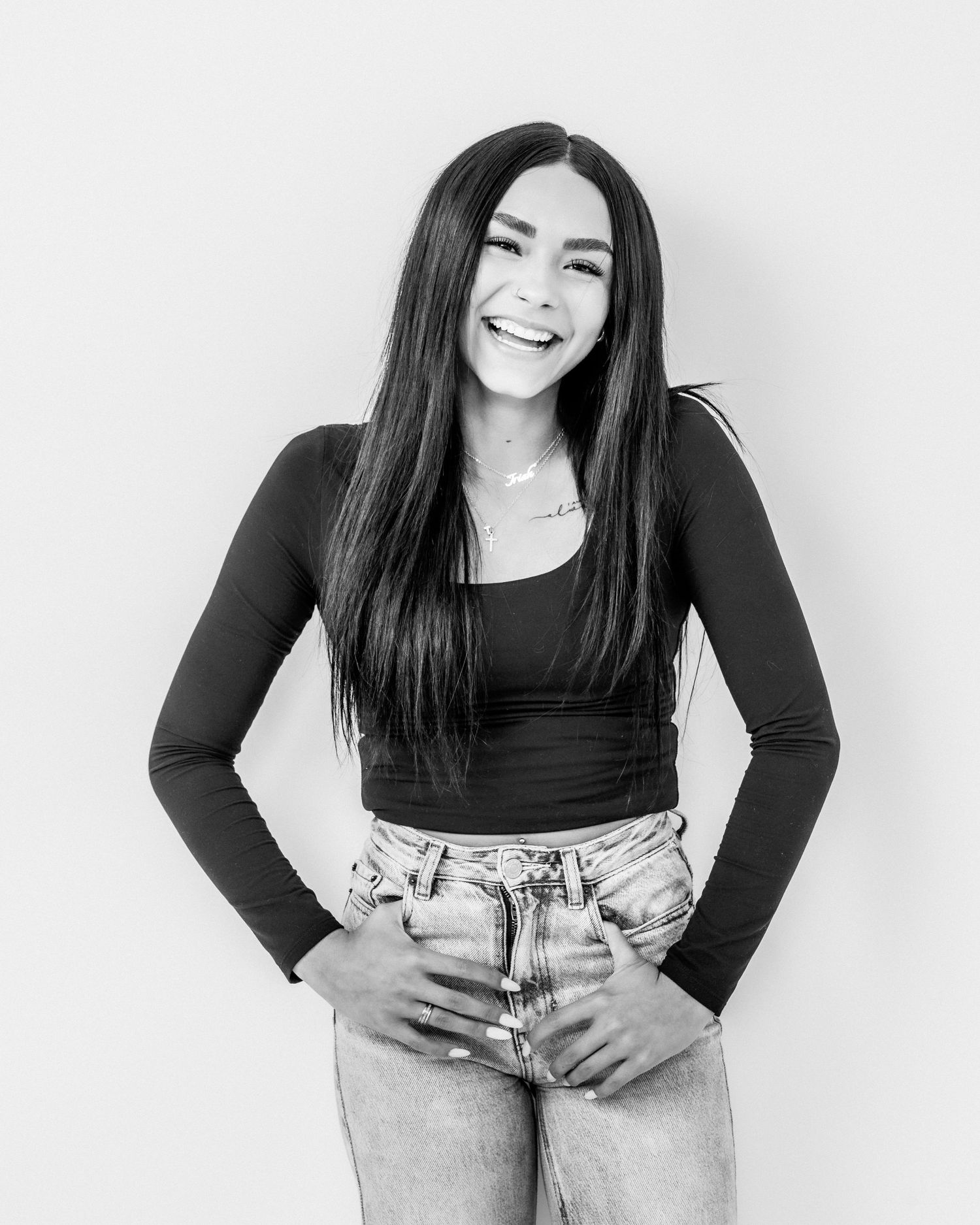 Black and white photo of a smiling young woman with long dark hair in jeans and black top.