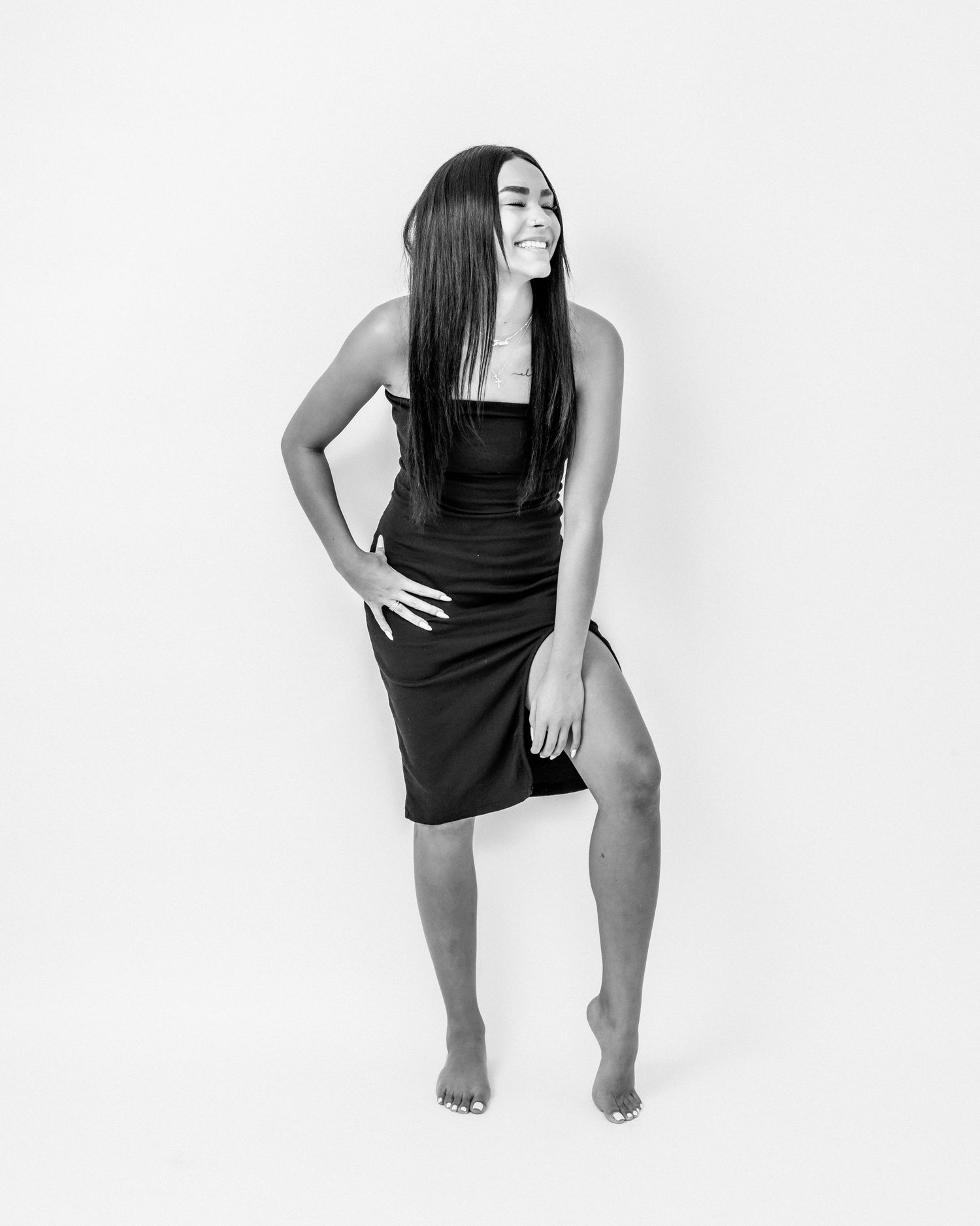 Black and white full-body portrait of a smiling woman in a black dress posing in a studio.