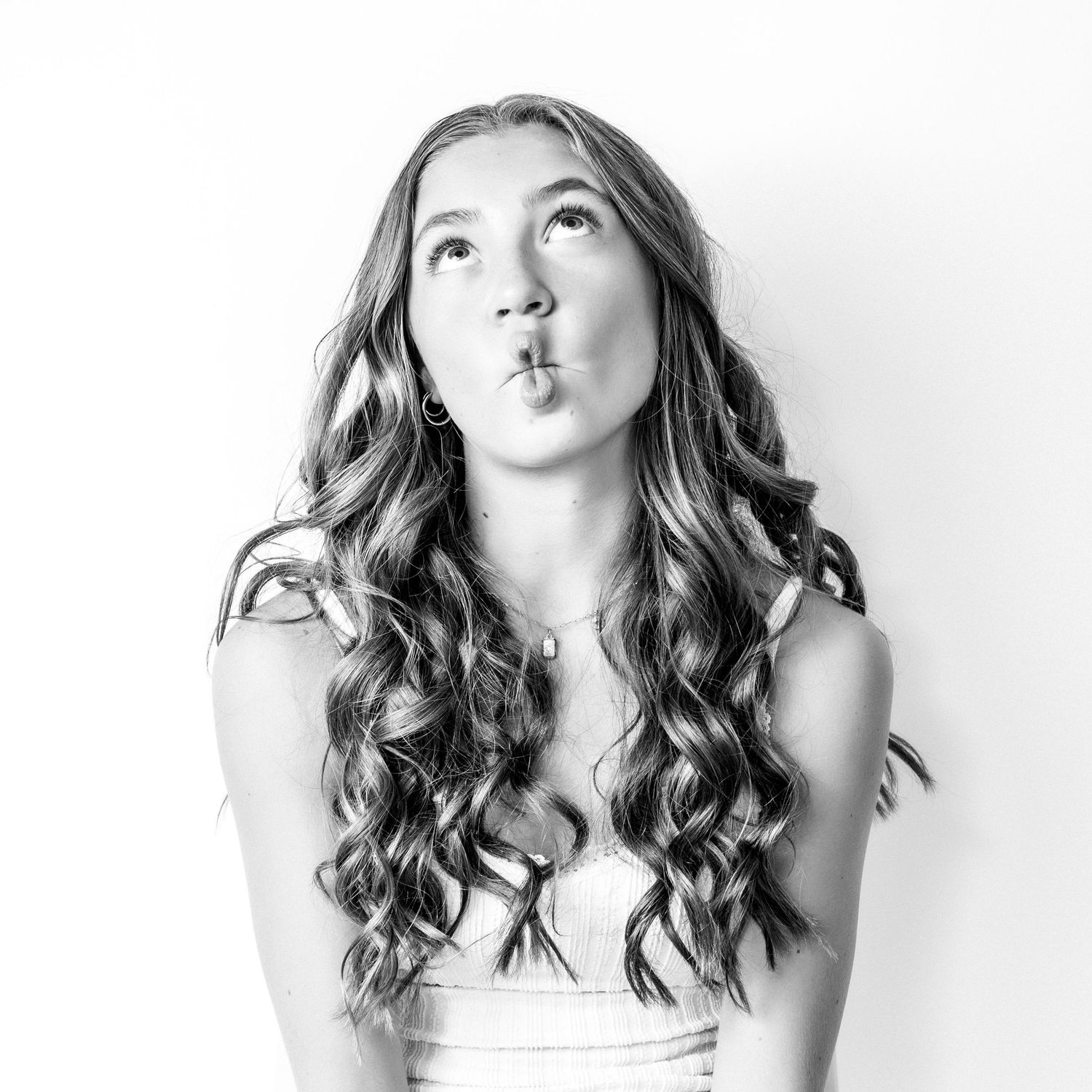 Black and white studio portrait of a curly-haired young woman making a playful kissing expression.