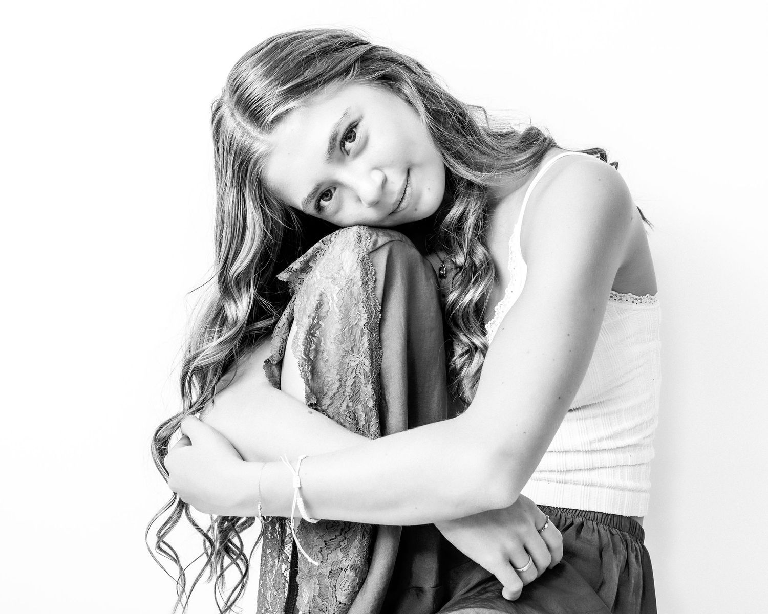 Black and white photo of a young girl hugging her knees and smiling softly.