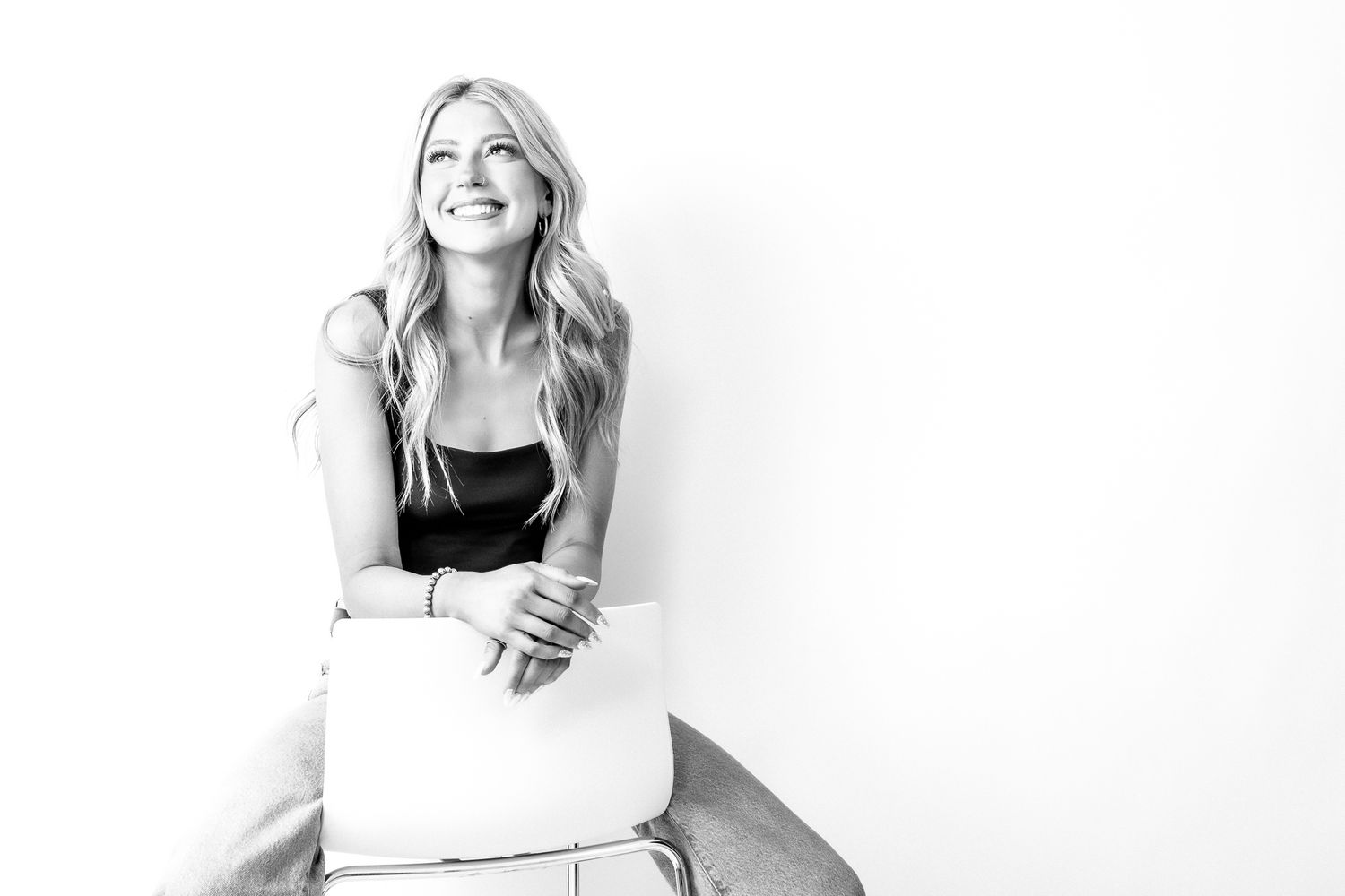 Smiling blonde woman sitting on a stool with a laptop, black and white portrait photo.