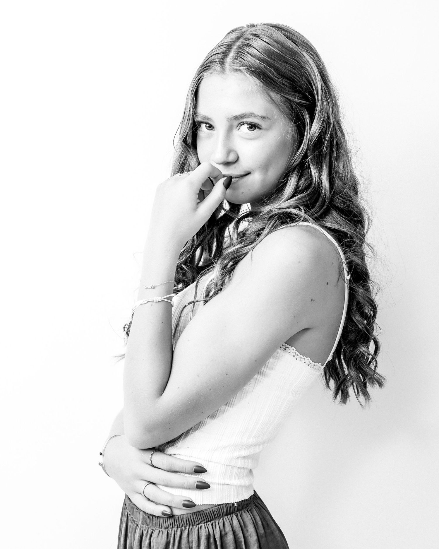 Black and white studio portrait of a young girl with long wavy hair posing with hand near face.